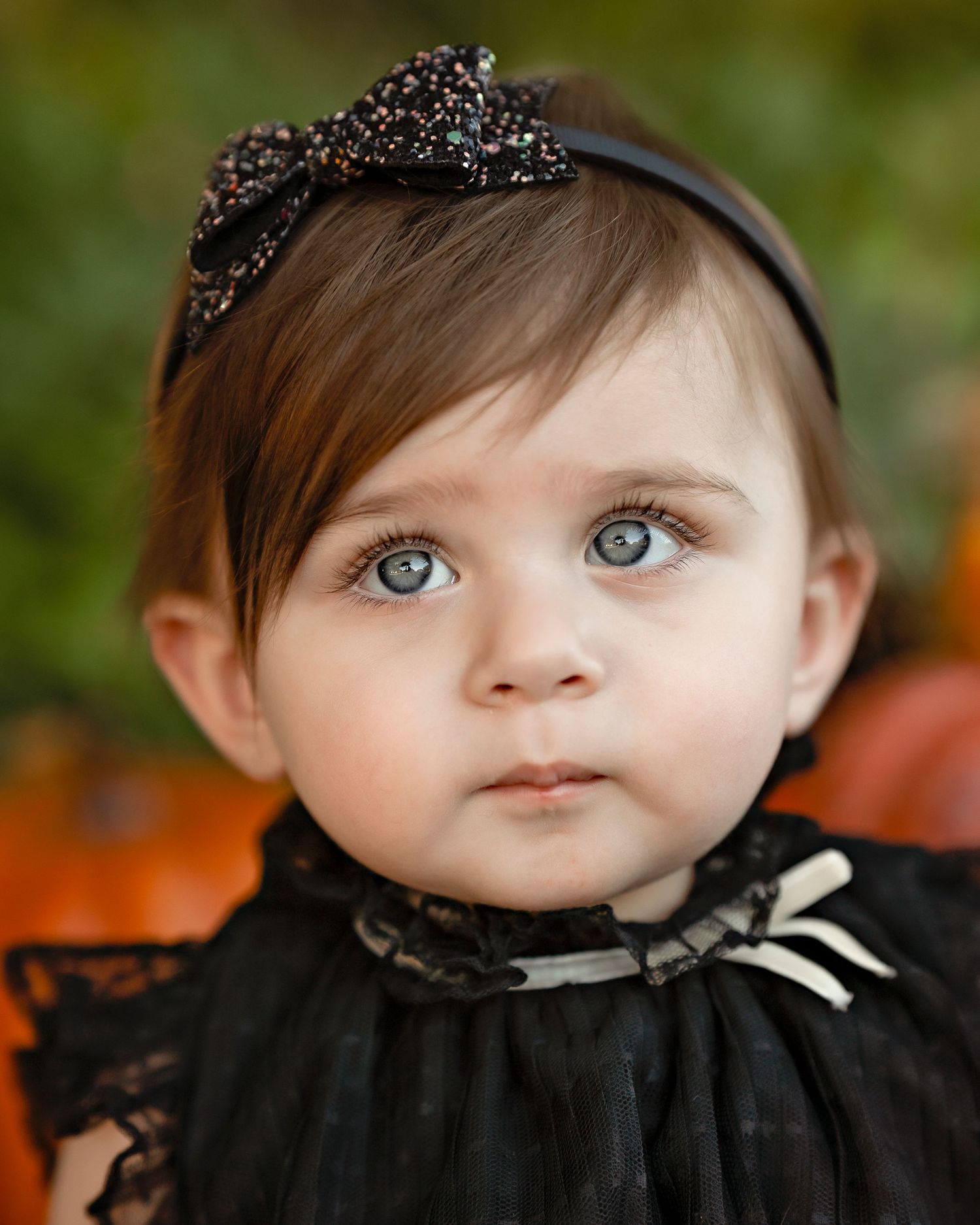 Close up portrait of a baby wearing a black headband with sparkly embellishments.