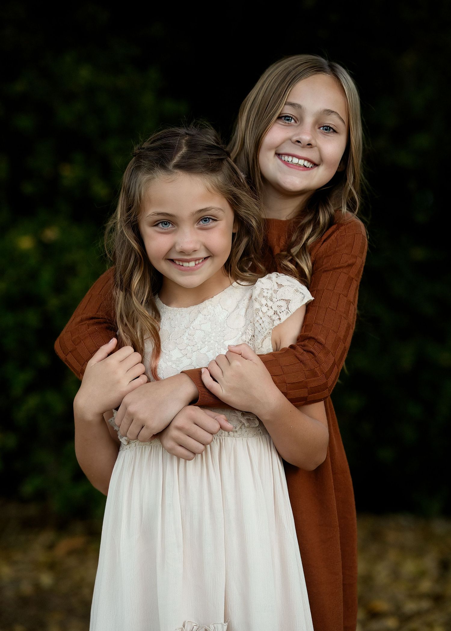 Sweet embrace between two people wearing white and brown clothing against dark background.