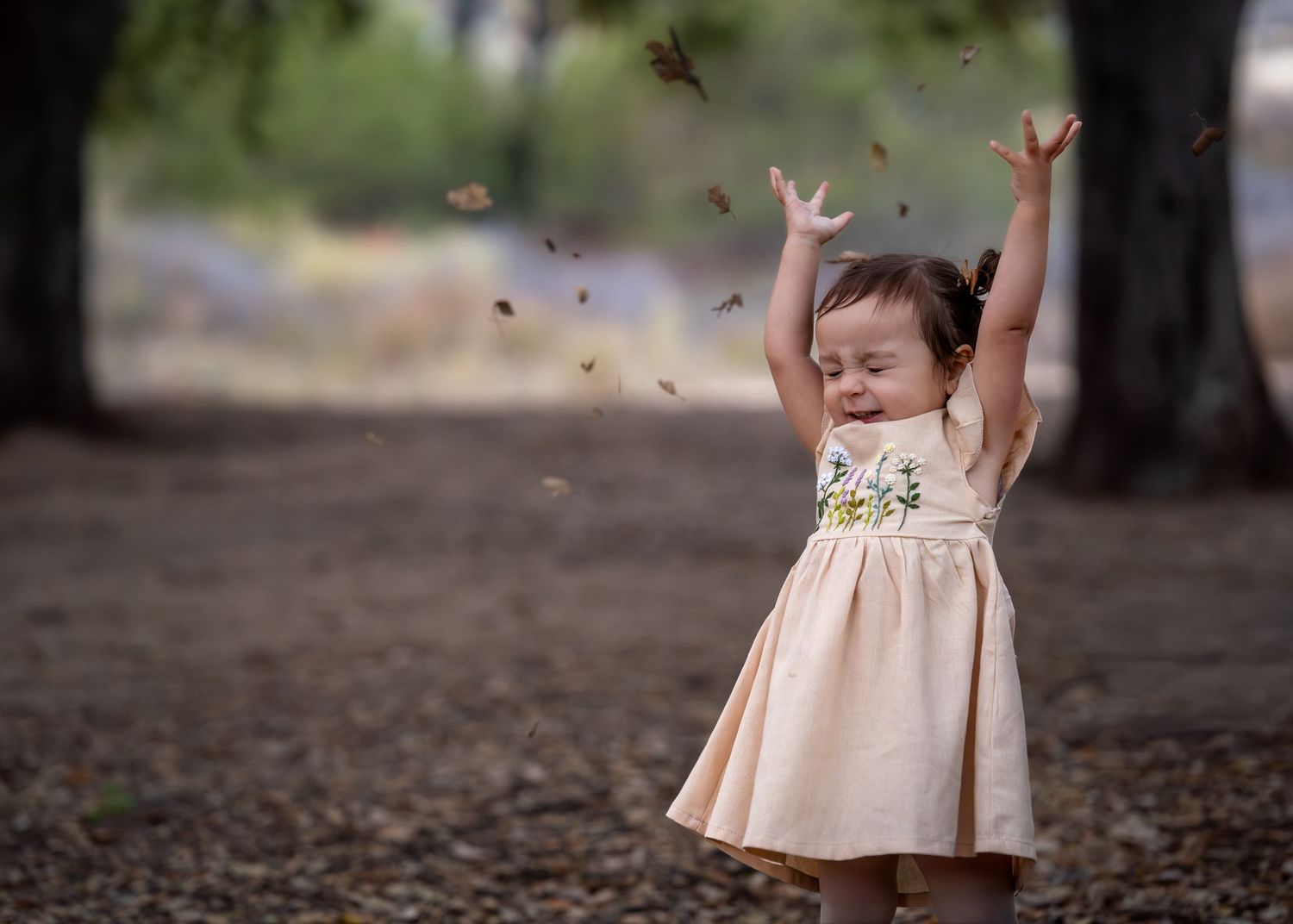 A child in a peach dress throws autumn leaves in the air.