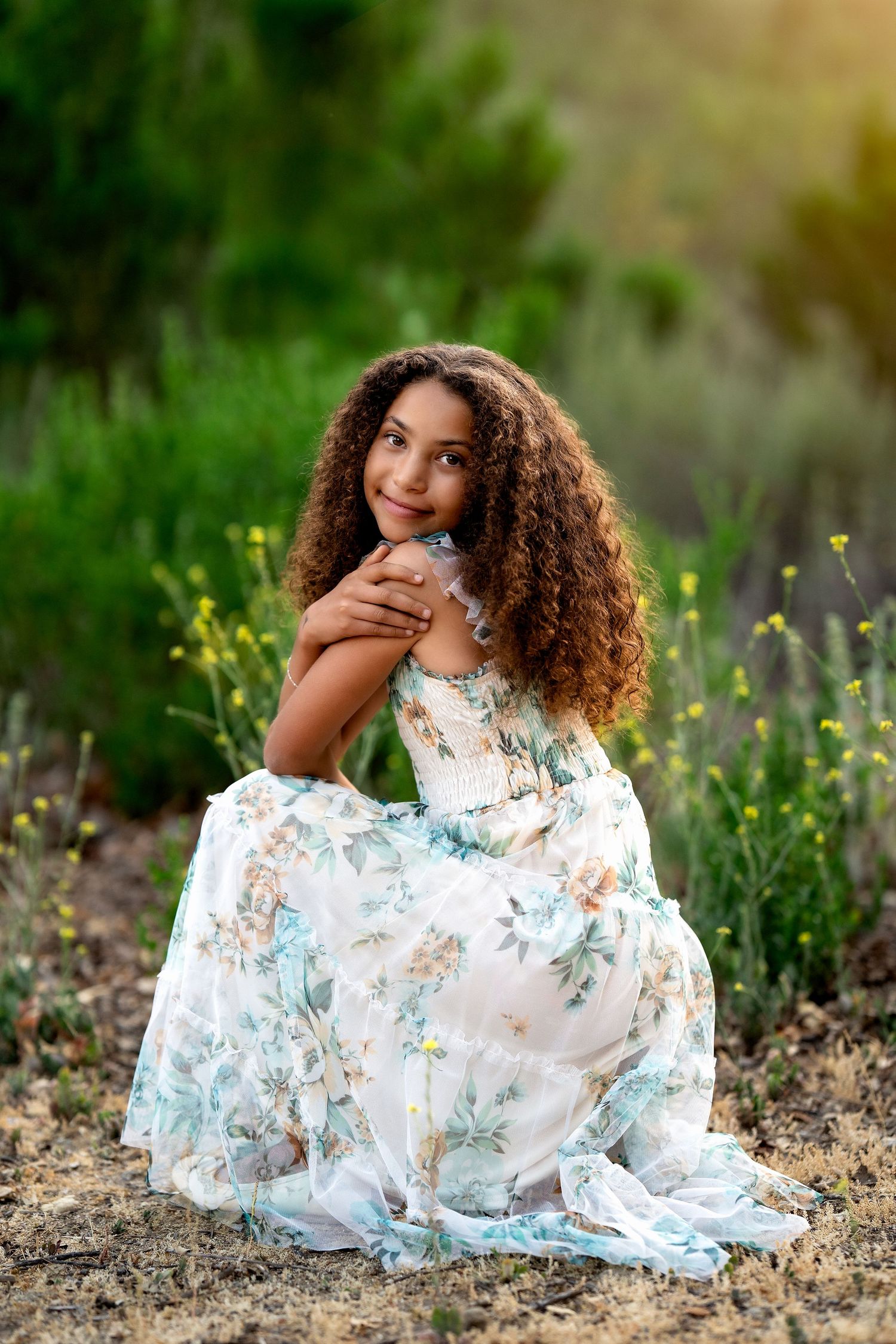 Person in a floral dress posing elegantly among wildflowers at sunset.