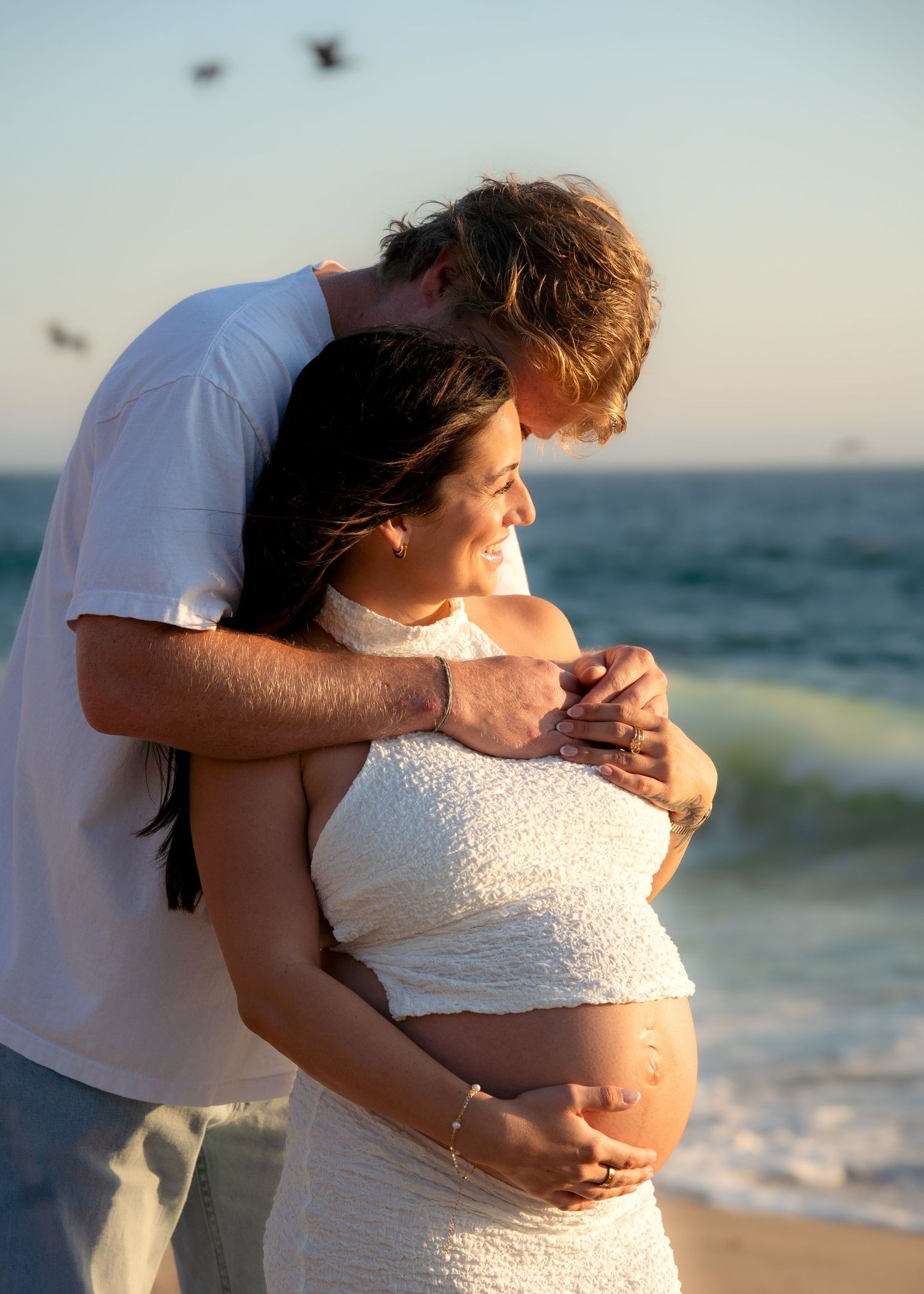 Tender moment captured during beach photoshoot with soft sunset lighting.
