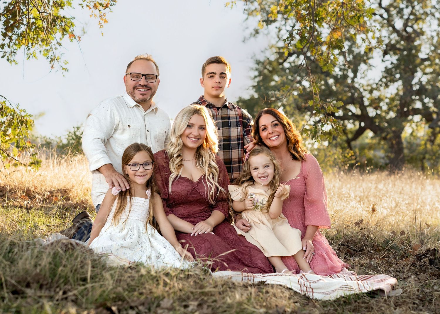 A family wearing coordinated burgundy and cream outfits poses together on grass during a golden hour photoshoot.