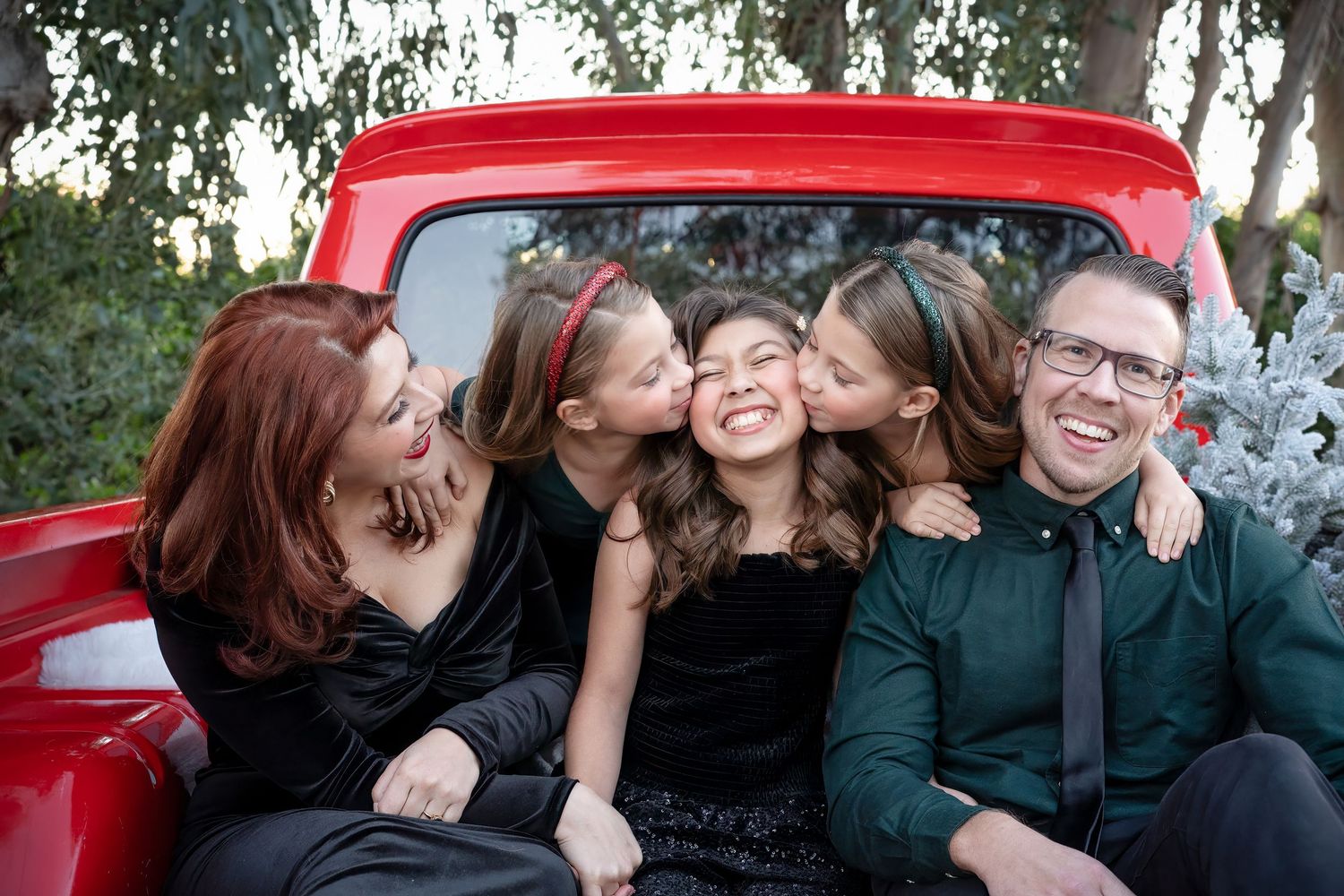 A group of friends laugh and embrace while posing together in front of a red car.