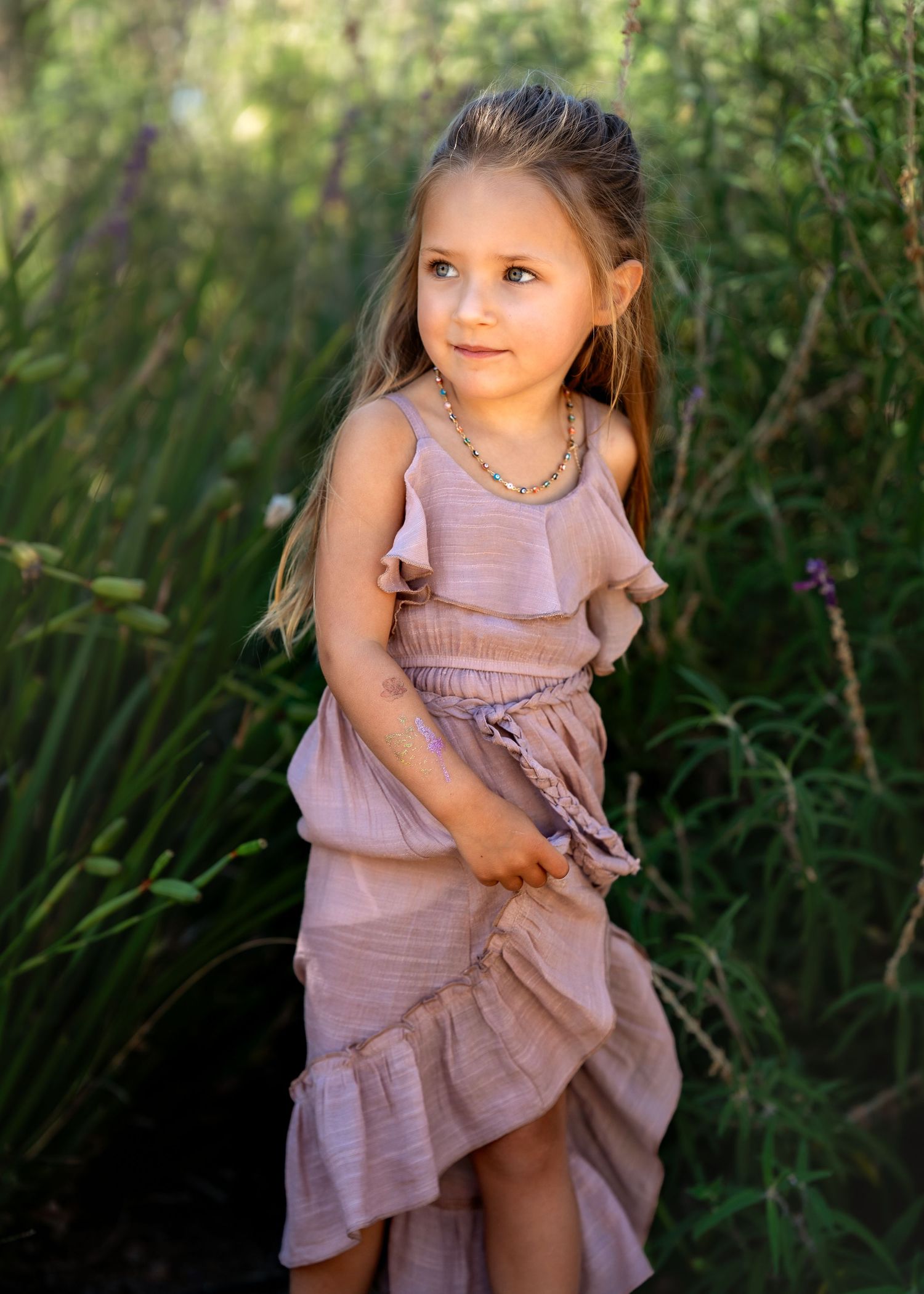 Whimsical outdoor portraits in lavender dress among garden greenery.