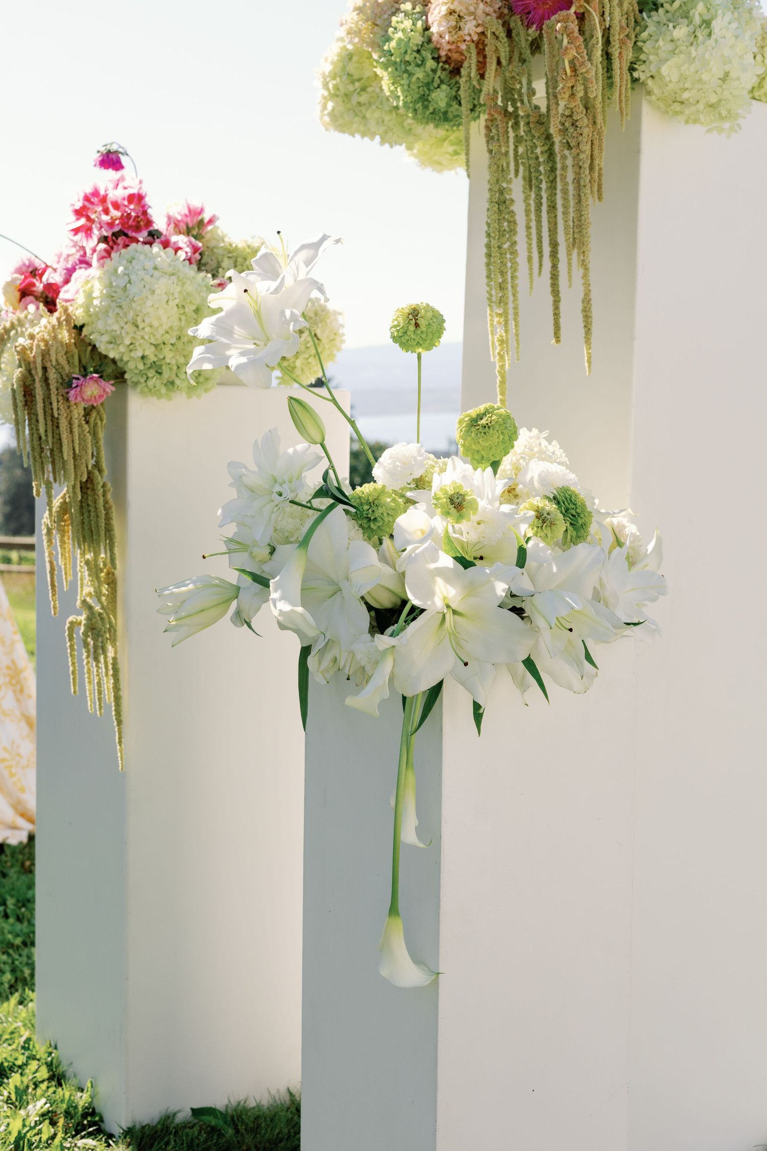 White wedding ceremony pillars decorated with white lilies, hydrangeas, and green allium flowers.