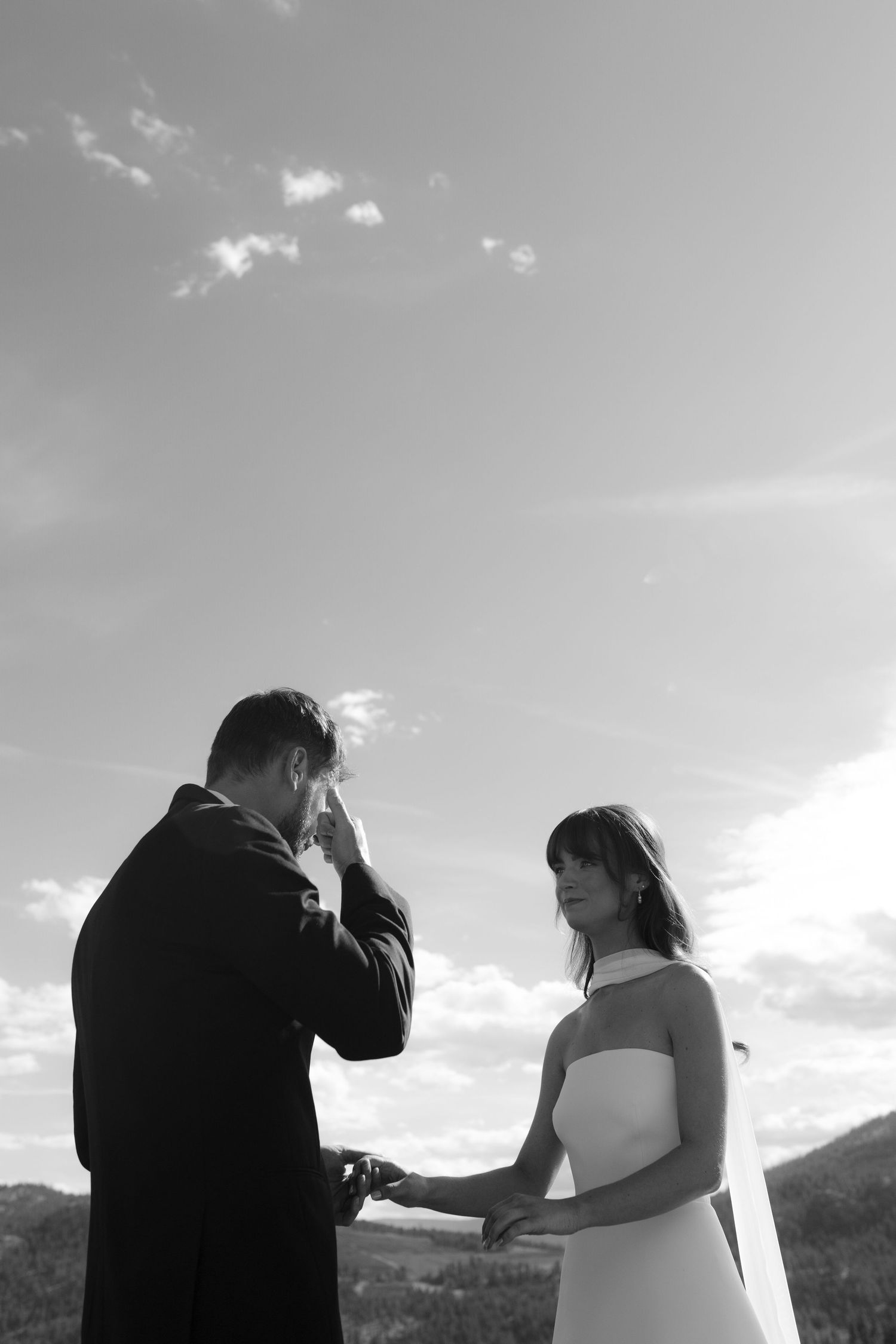 Black and white photo of emotional groom wiping tears during outdoor wedding ceremony.