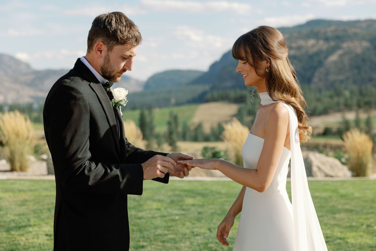 Groom slides wedding ring onto brides finger during outdoor mountain ceremony.