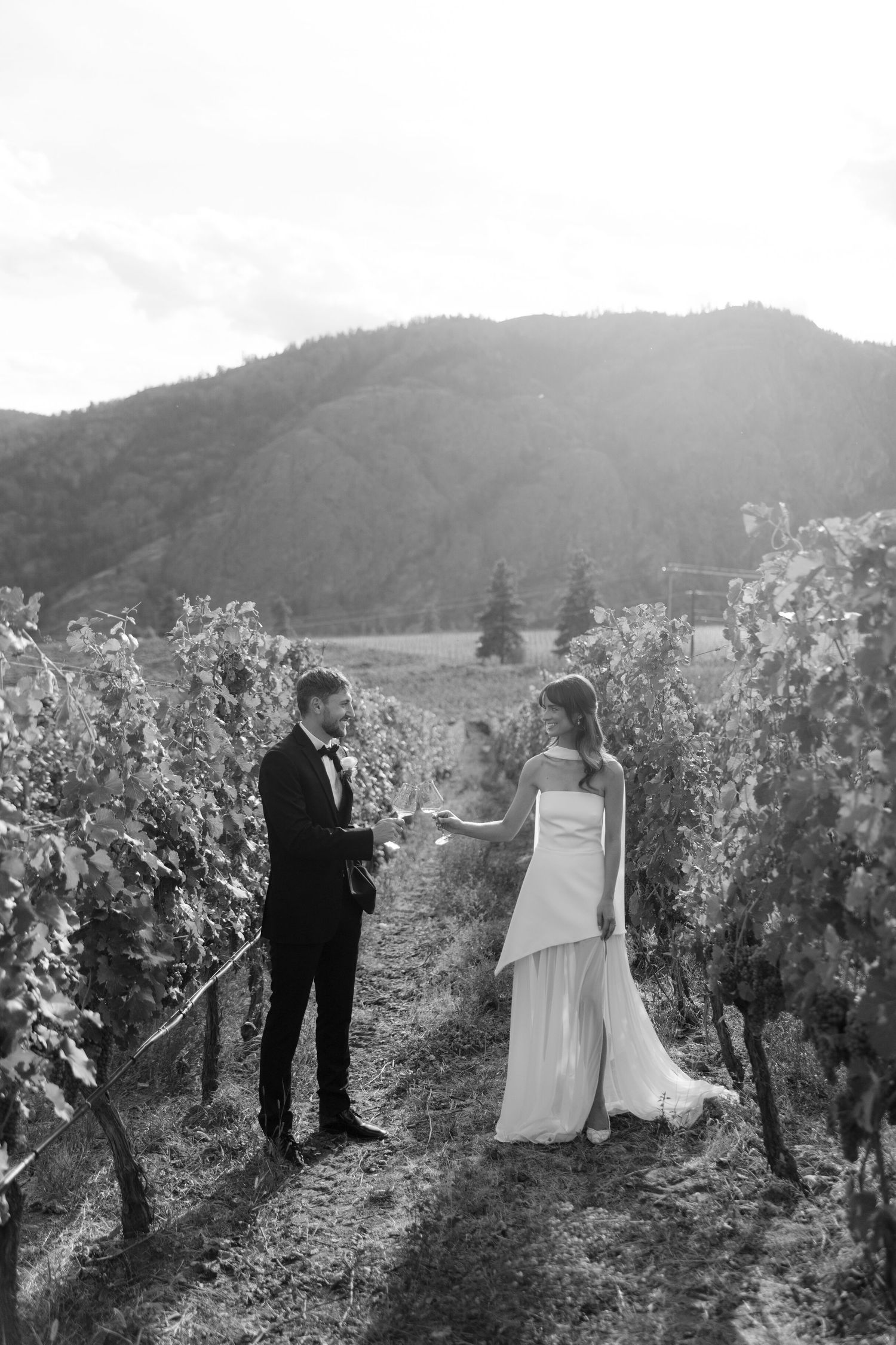Bride and groom share a romantic moment in a vineyard with mountain backdrop in black and white.