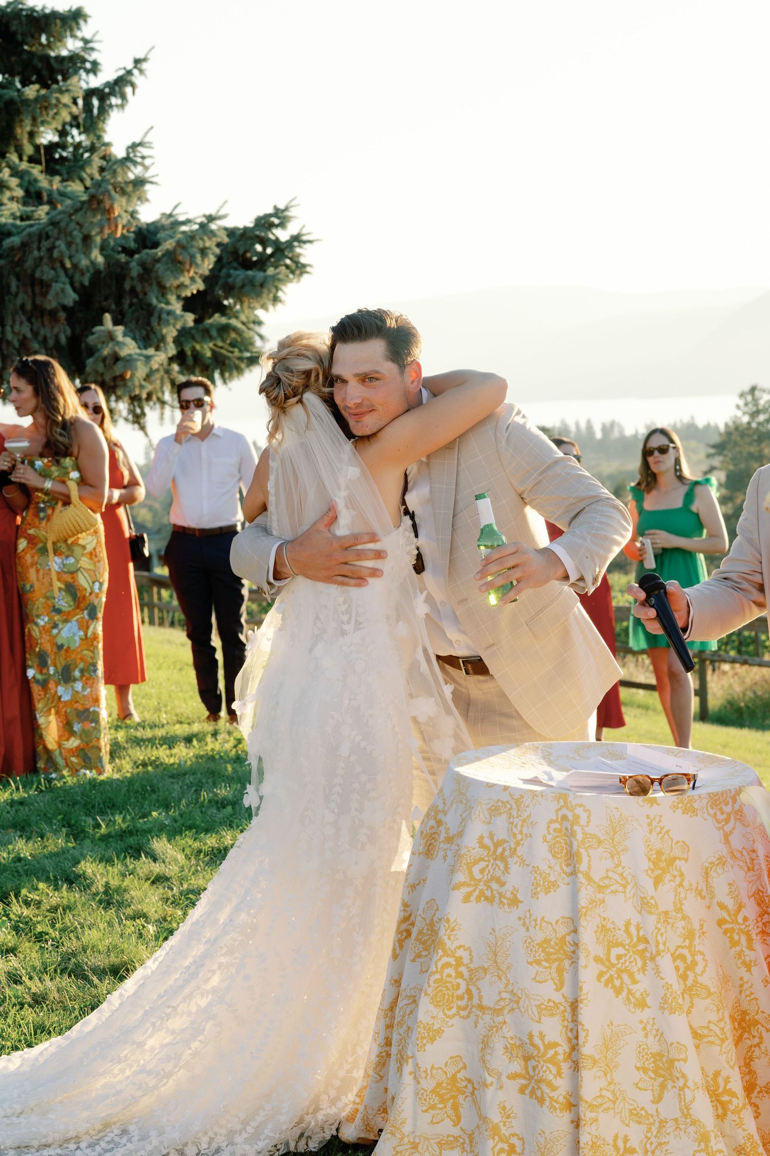 Bride and groom share a warm embrace outdoors at their wedding reception on a sunny day.