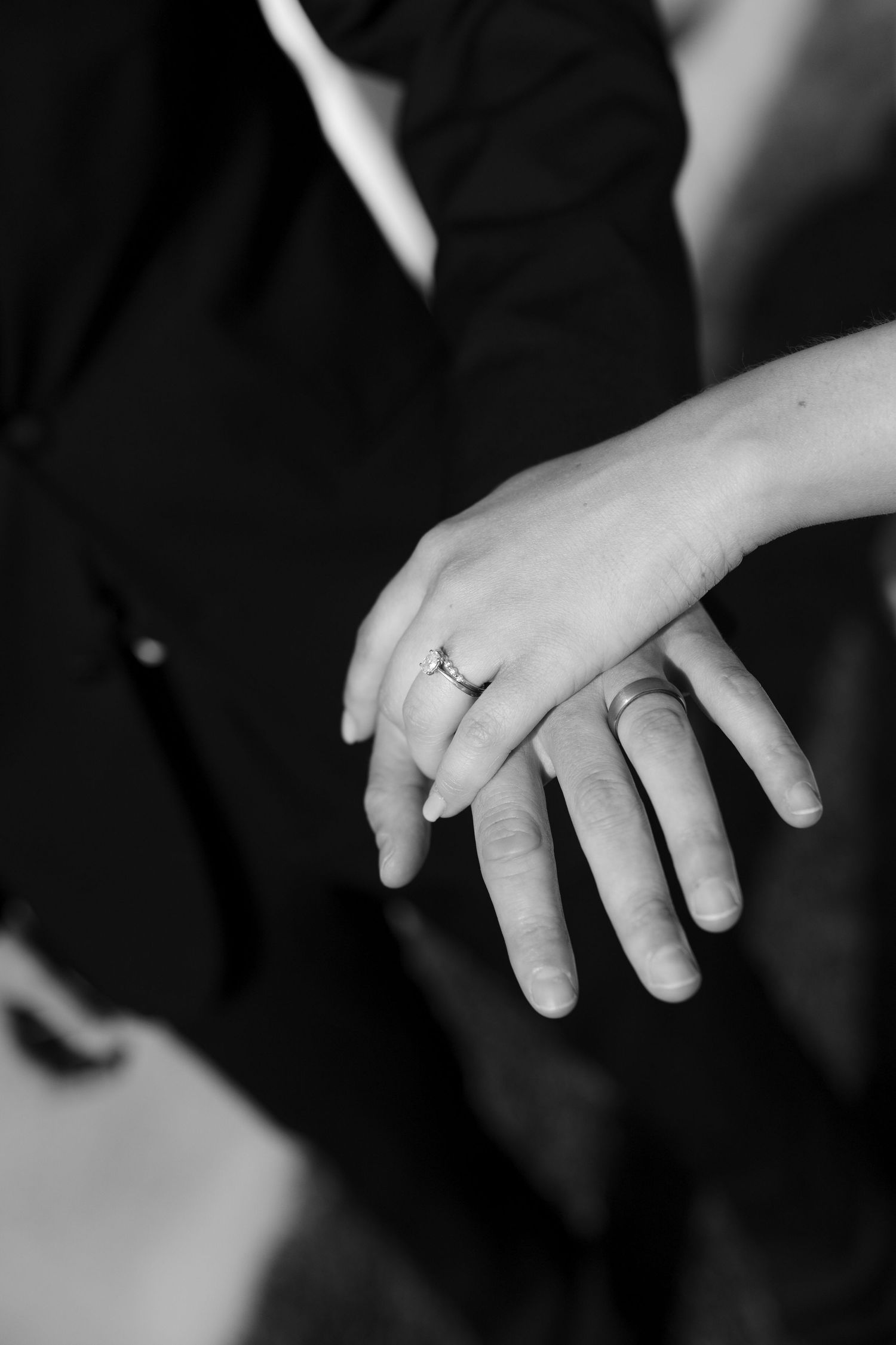 Black and white close-up of newlyweds hands displaying wedding and engagement rings.
