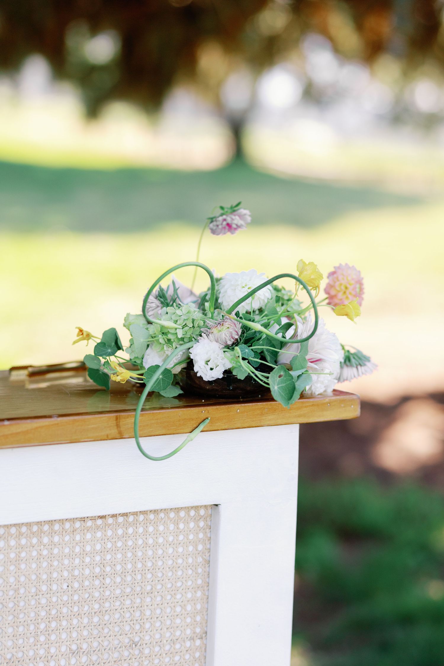 Delicate floral centerpiece with white roses and greenery on wooden display cabinet outdoors.