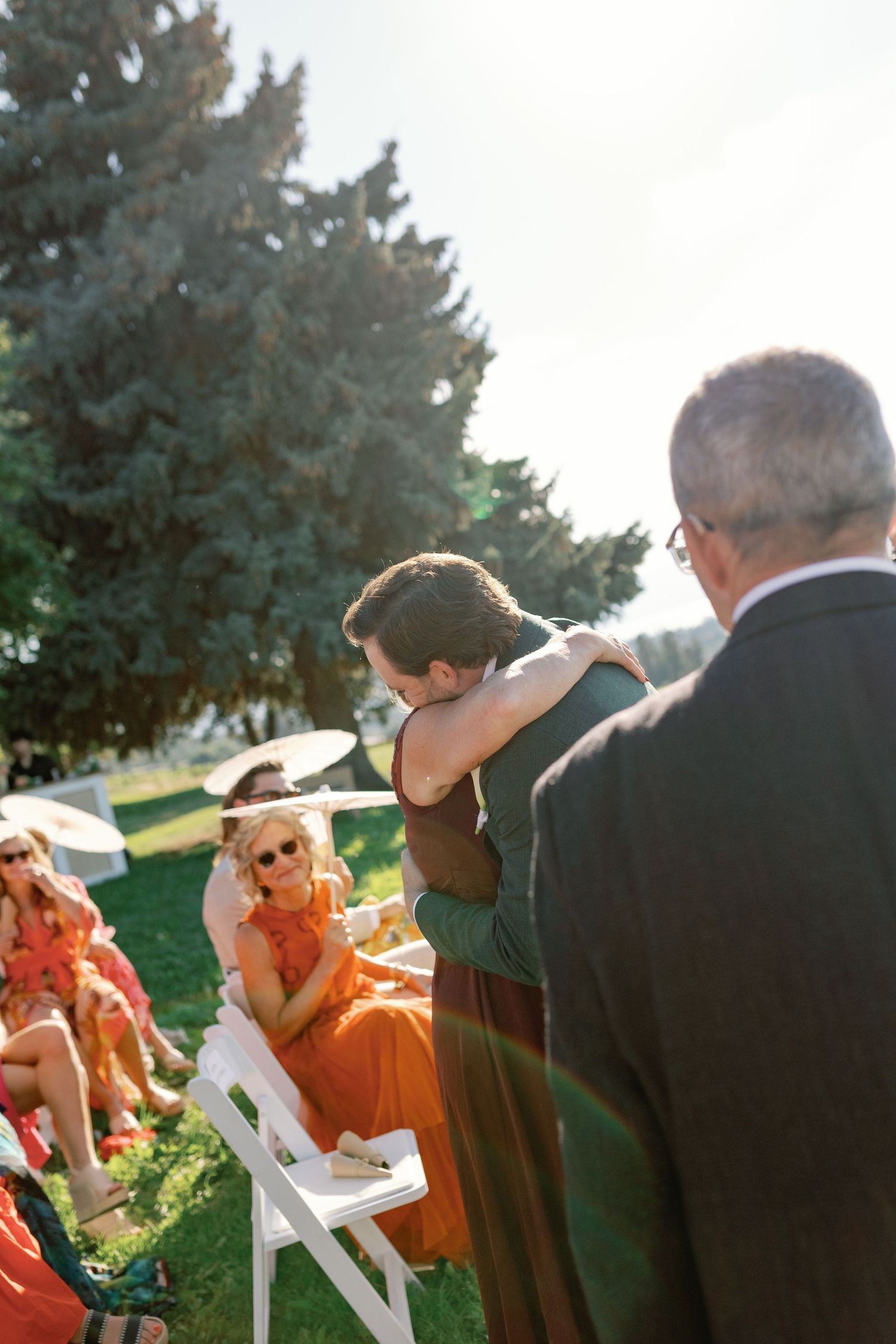 Groom embracing a guest while walking down the aisle at an outdoor wedding ceremony.