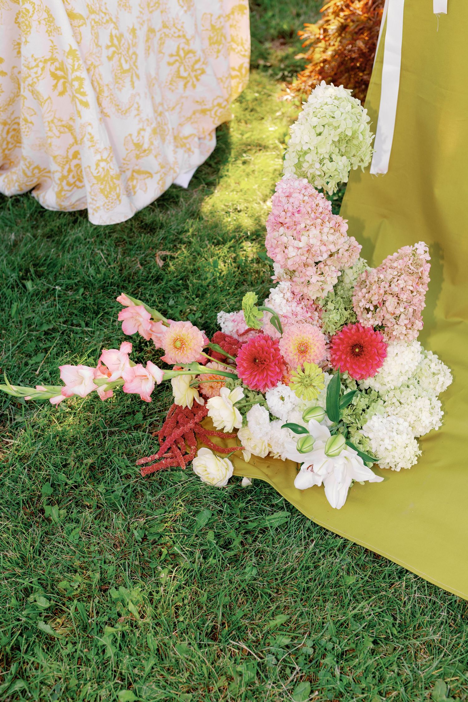 Colorful wedding floral arrangement on grass featuring pink hydrangeas, gerbera daisies, and white lilies.