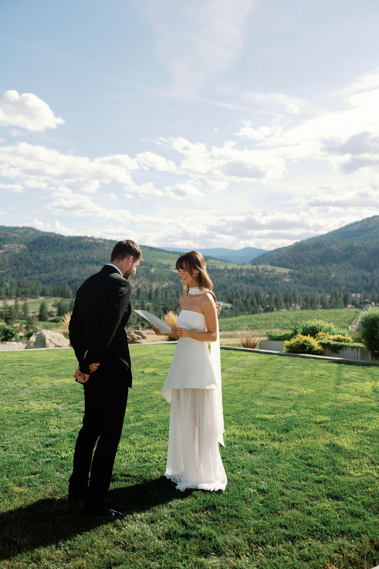 Elegant bride reads vows to groom outdoors with breathtaking mountain and valley views behind them.