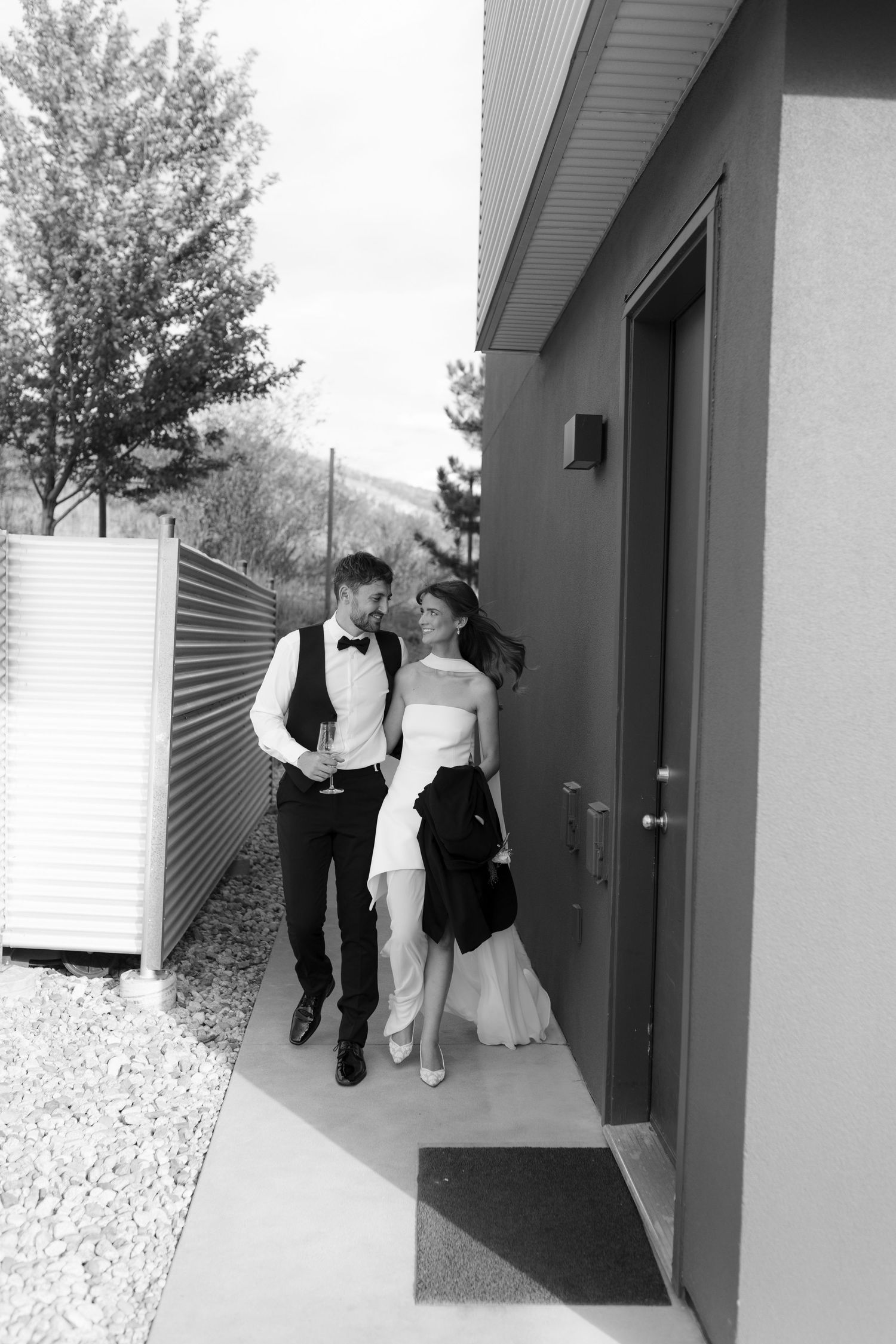 Black and white photo of bride and groom walking together outside modern venue building.