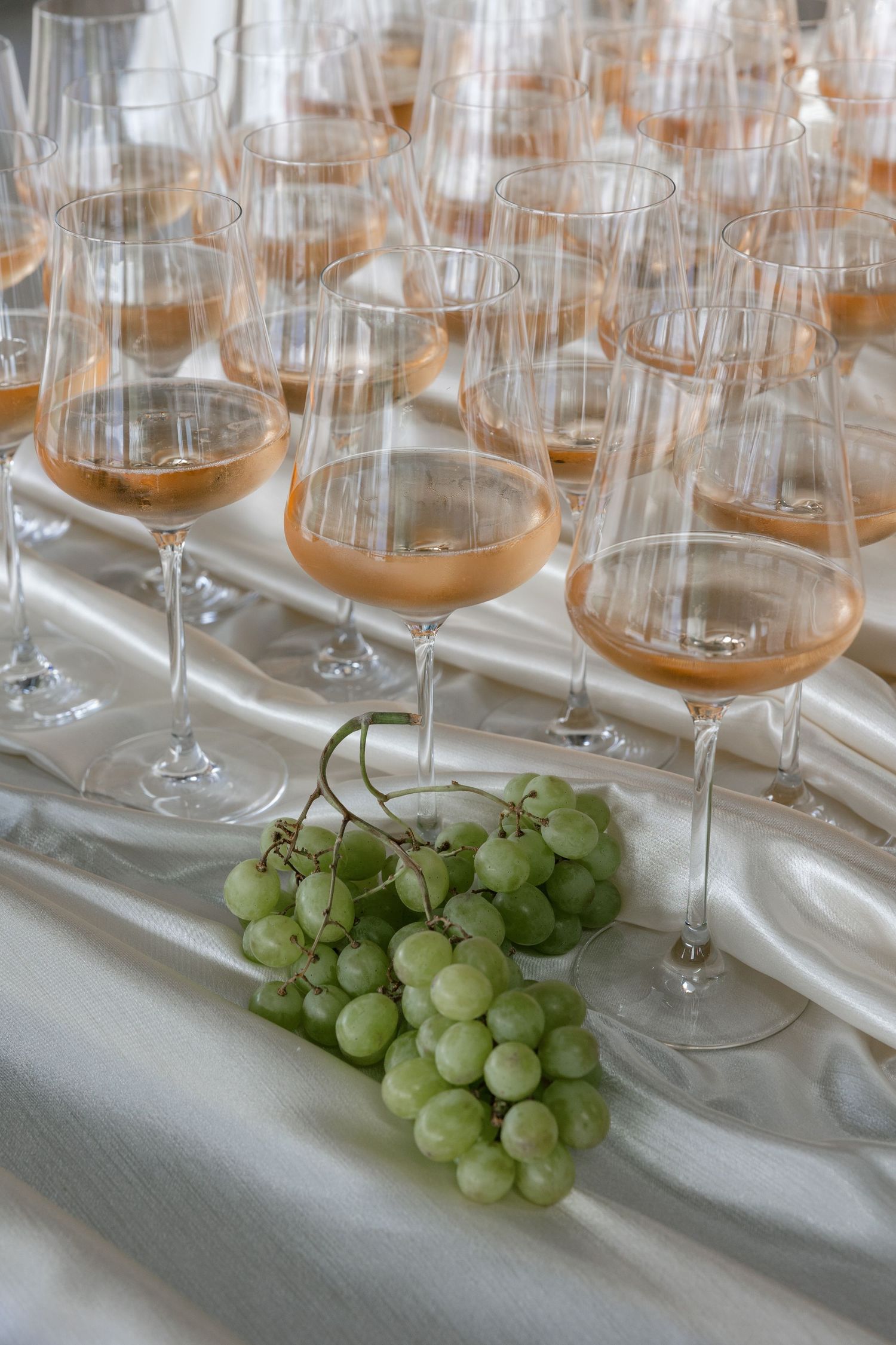 Elegant wine glasses filled with rosé on a white tablecloth, with fresh green grapes in the foreground.