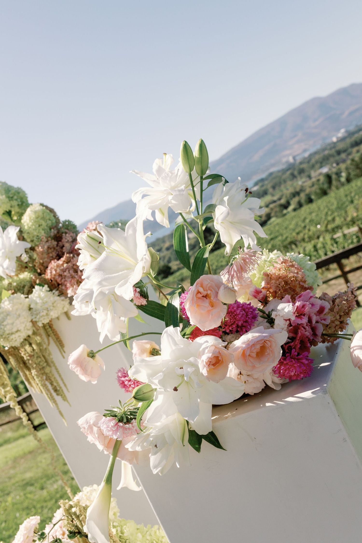 Elegant outdoor wedding floral arrangement with white lilies and pink roses against mountain backdrop.