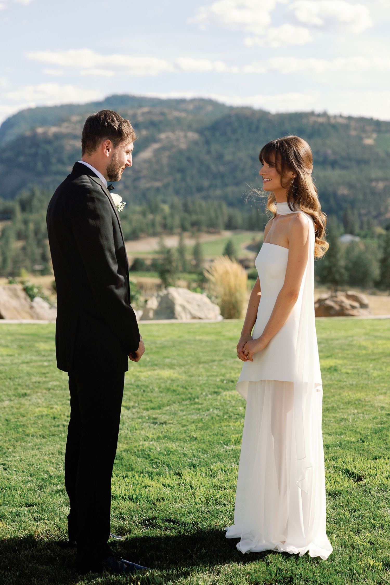 Smiling bride and groom face each other during outdoor wedding ceremony in mountains.