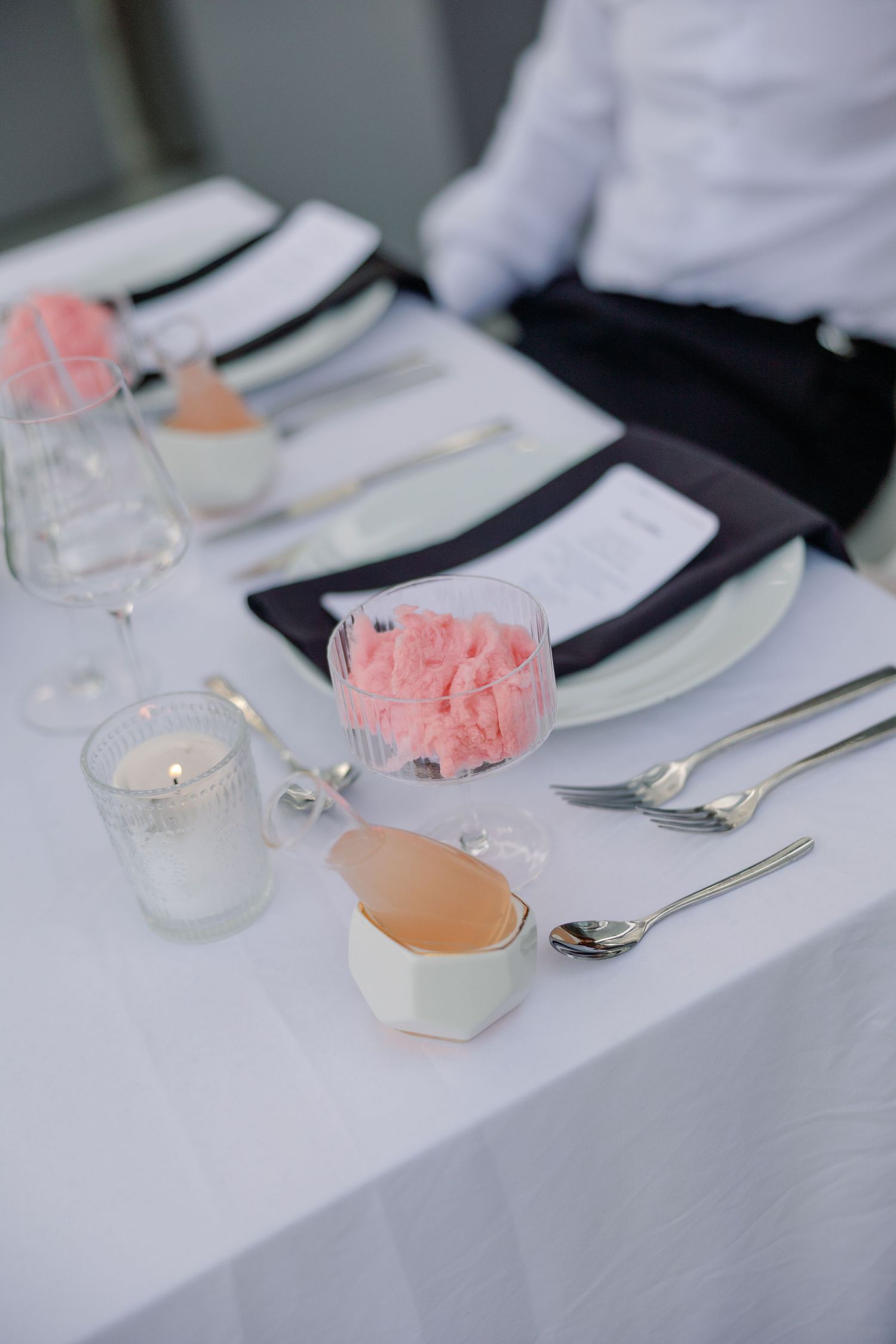 Elegant wedding table setting with pink sorbet, candles, silverware and dark napkins.