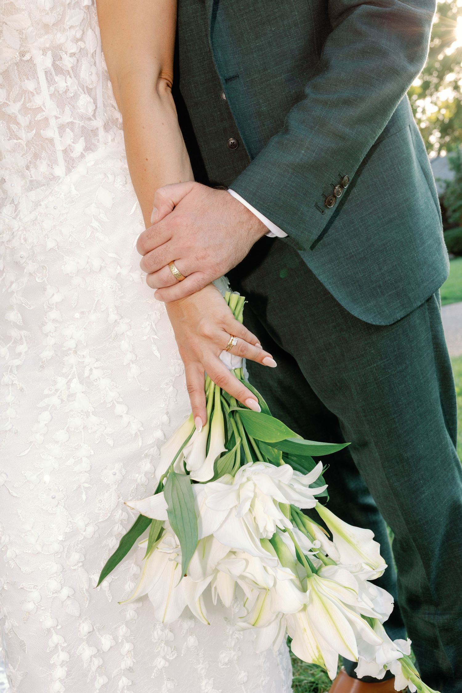 Close-up of newlyweds hands with wedding rings holding white tulip bouquet.
