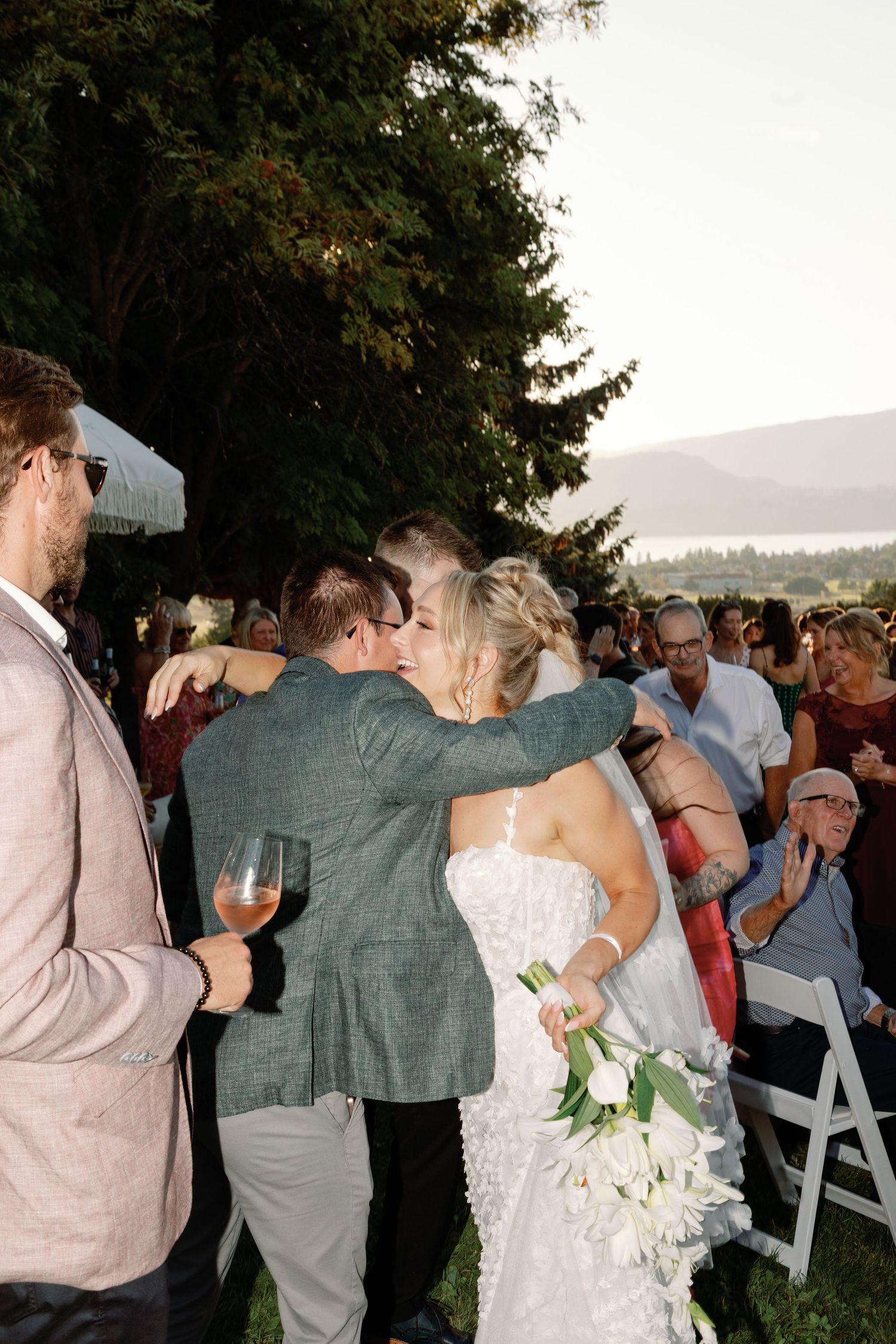 Bride holding white tulips hugs a guest during outdoor wedding ceremony celebrations.
