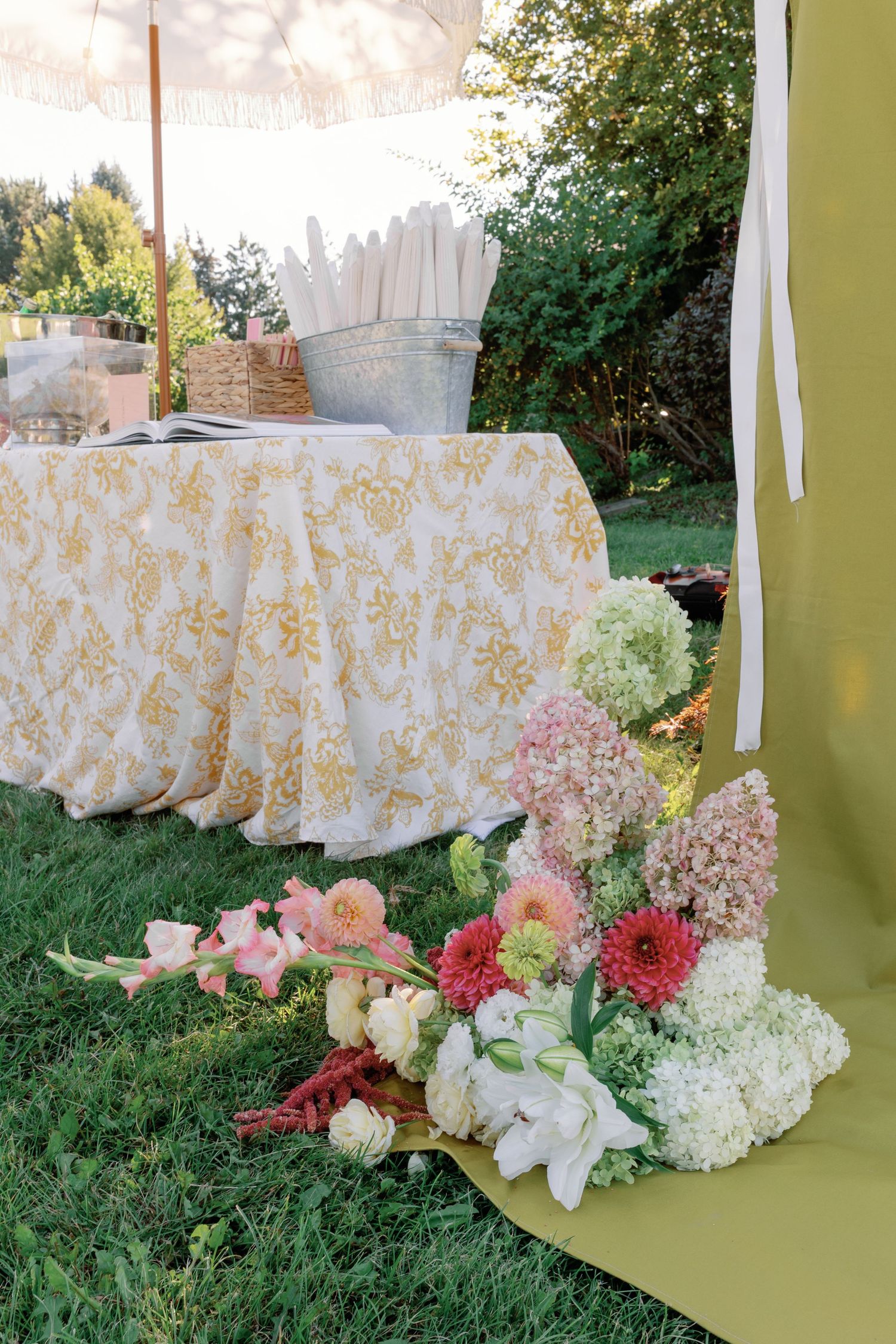 Elegant outdoor wedding table with gold floral tablecloth and colorful flower arrangements on grass.