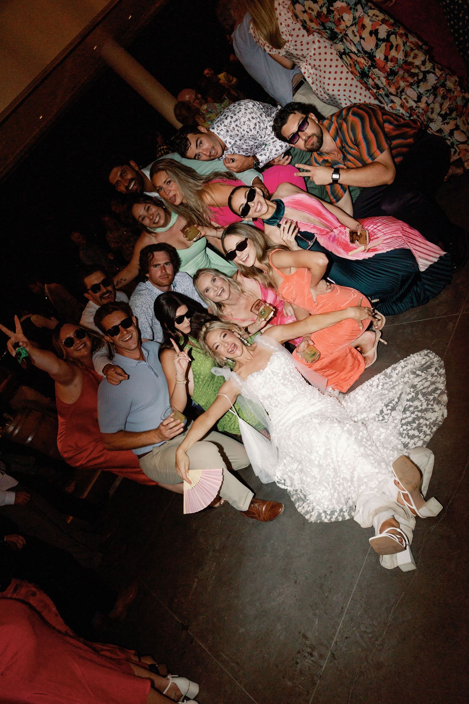 Bride poses with large group of wedding guests lying on the floor.