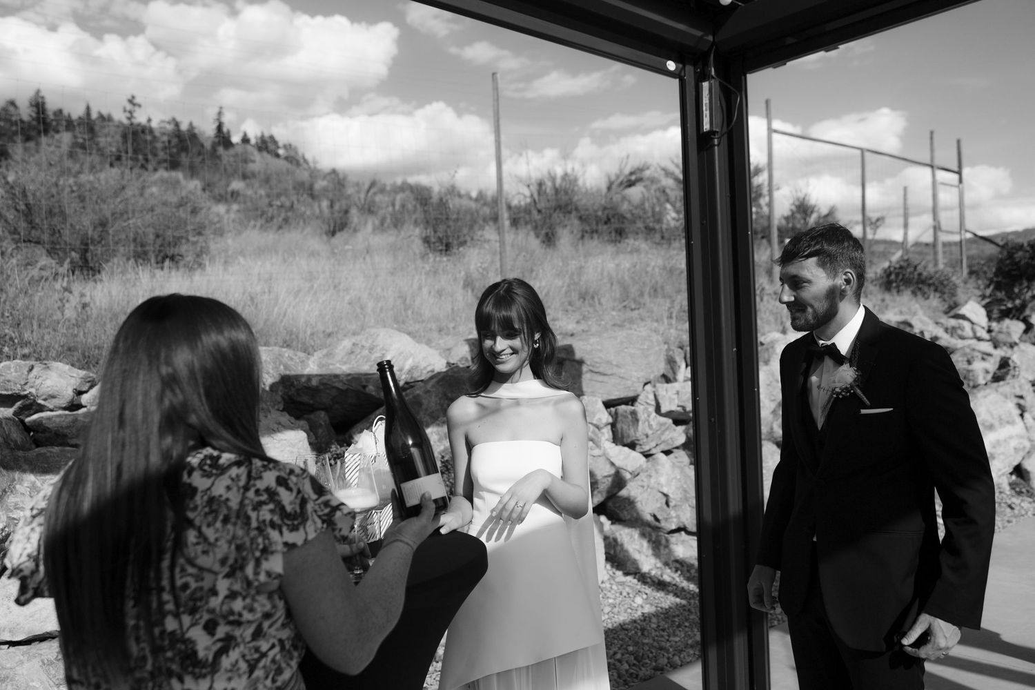 Black and white photo of officiant pouring champagne for bride and groom at ceremony.