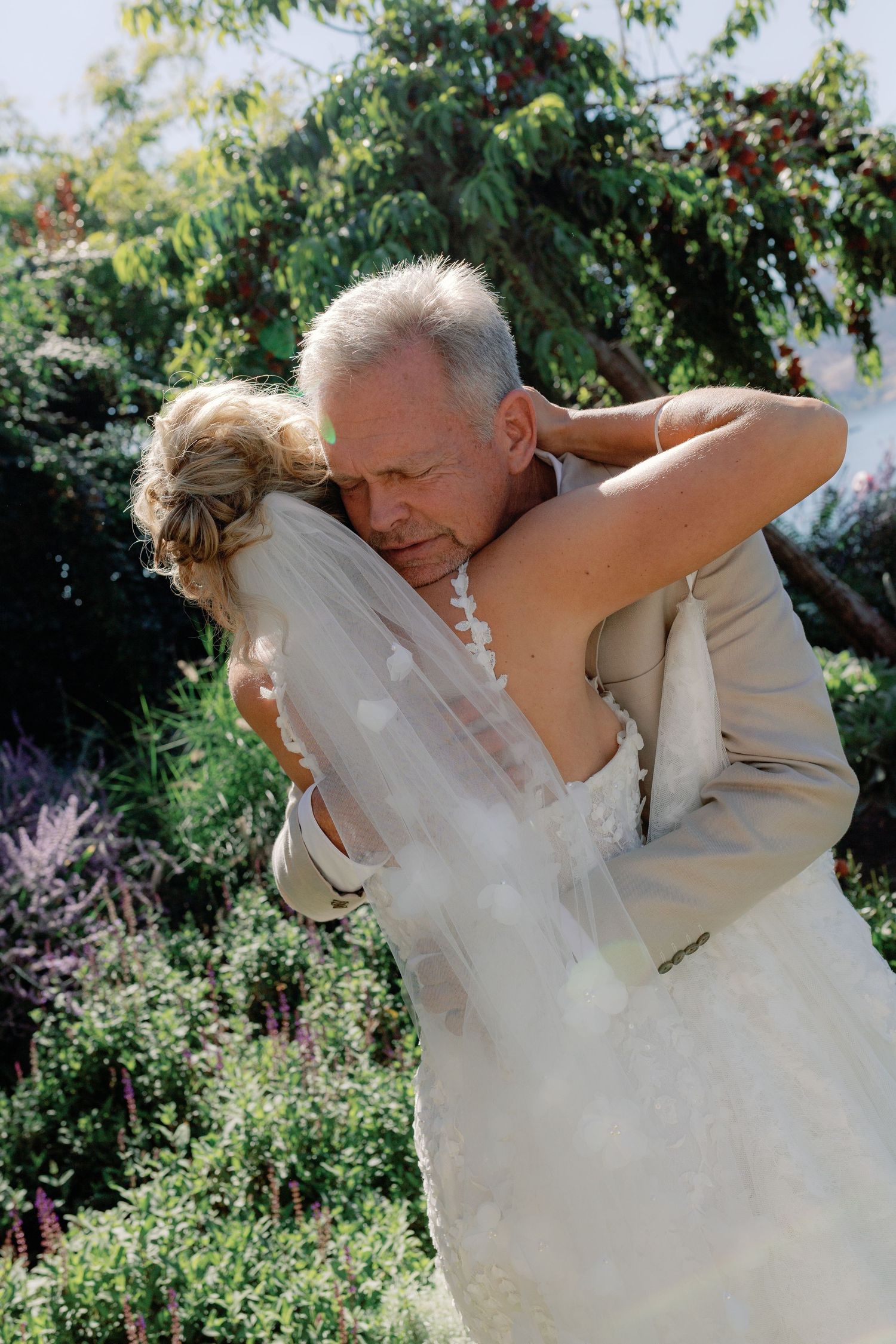 Emotional father of the bride hugging daughter in wedding gown during heartfelt first look in garden setting.