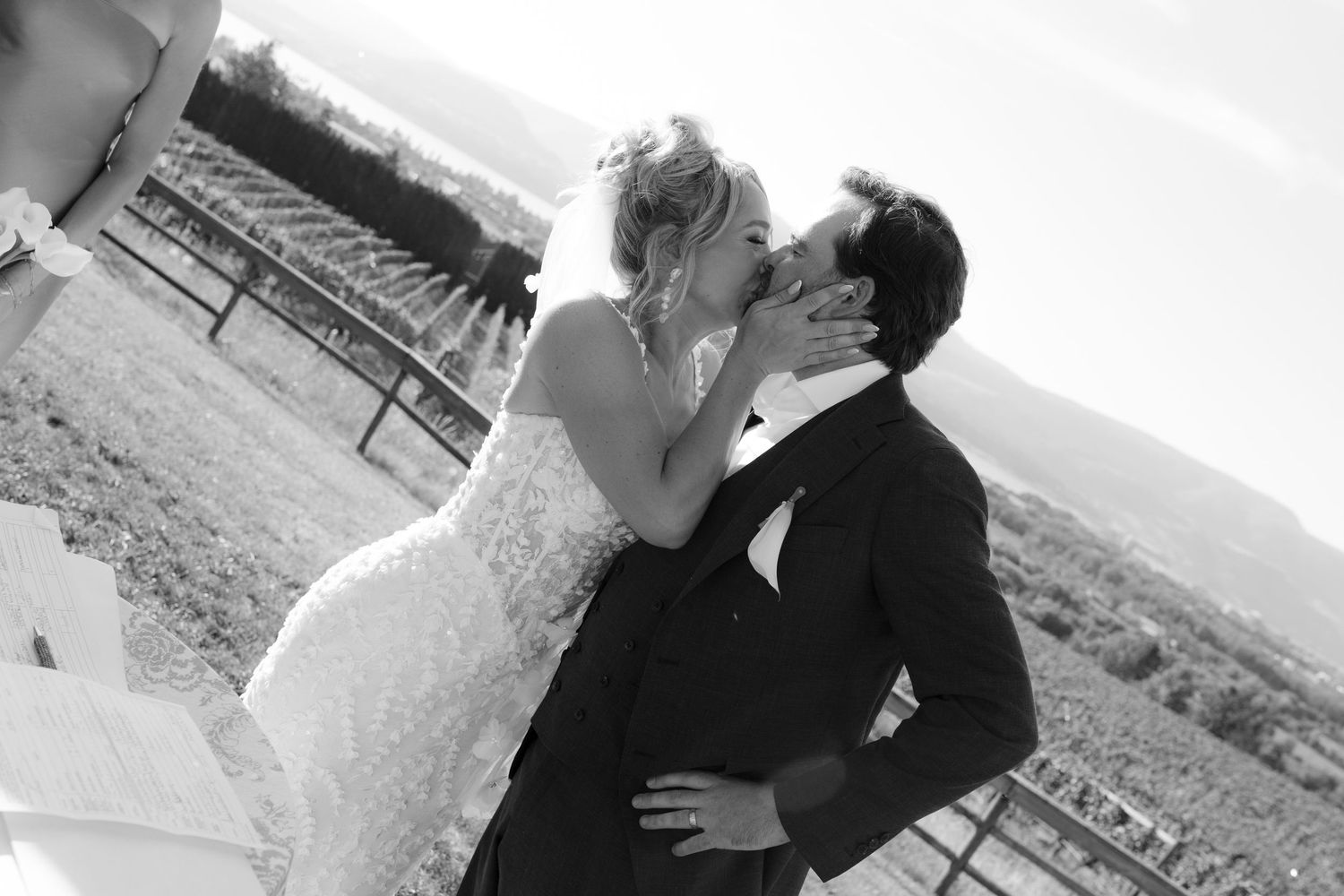 Black and white photo of bride and groom sharing romantic first kiss at vineyard wedding.