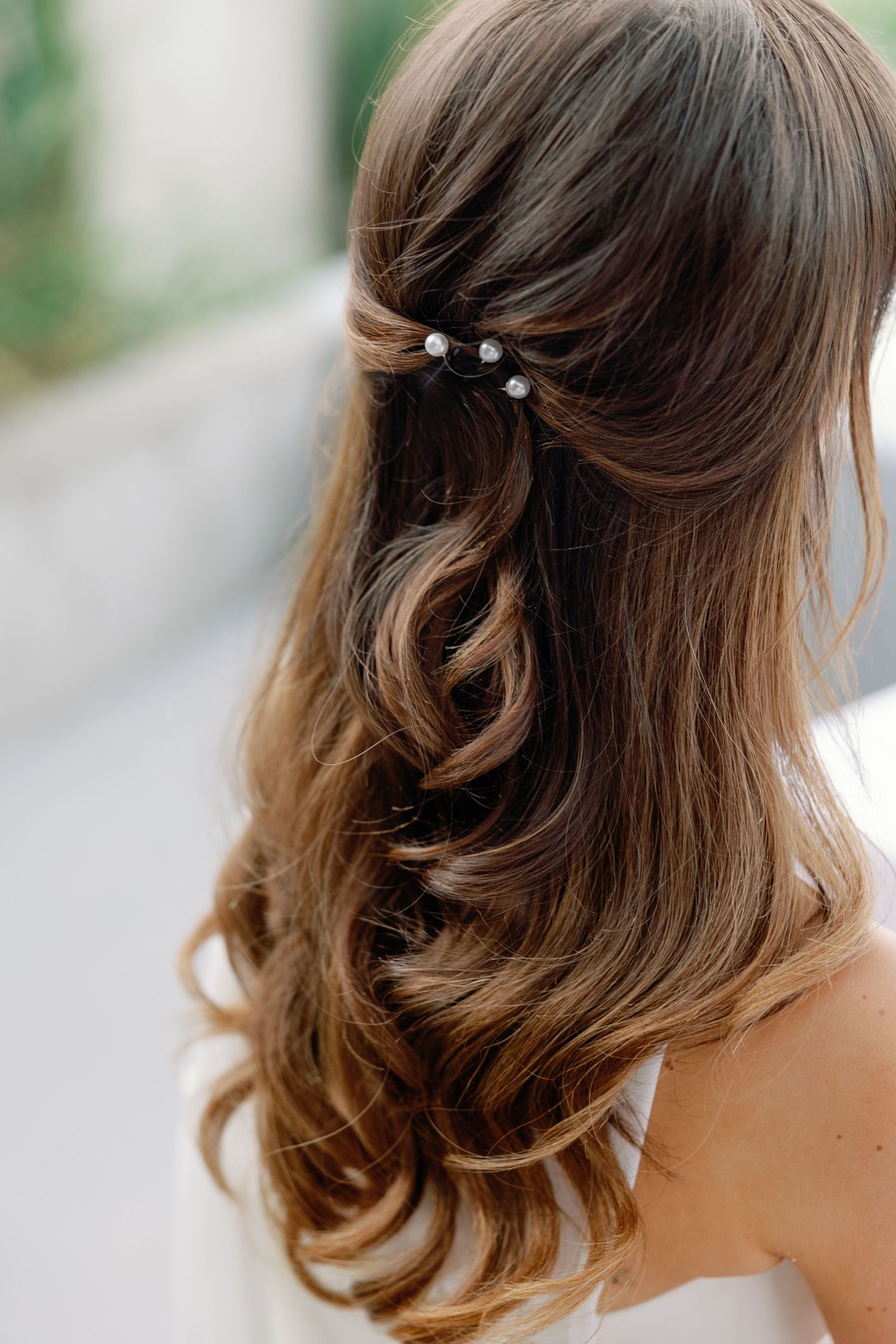 Close-up of bride's elegant half-up hairstyle with soft curls and delicate pearl hair pins on wedding day.