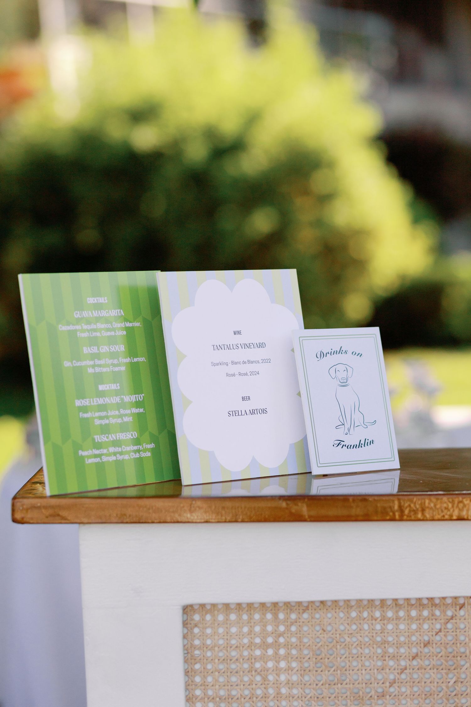 Wedding ceremony programs and menu cards displayed on wooden cabinet at outdoor vineyard wedding.