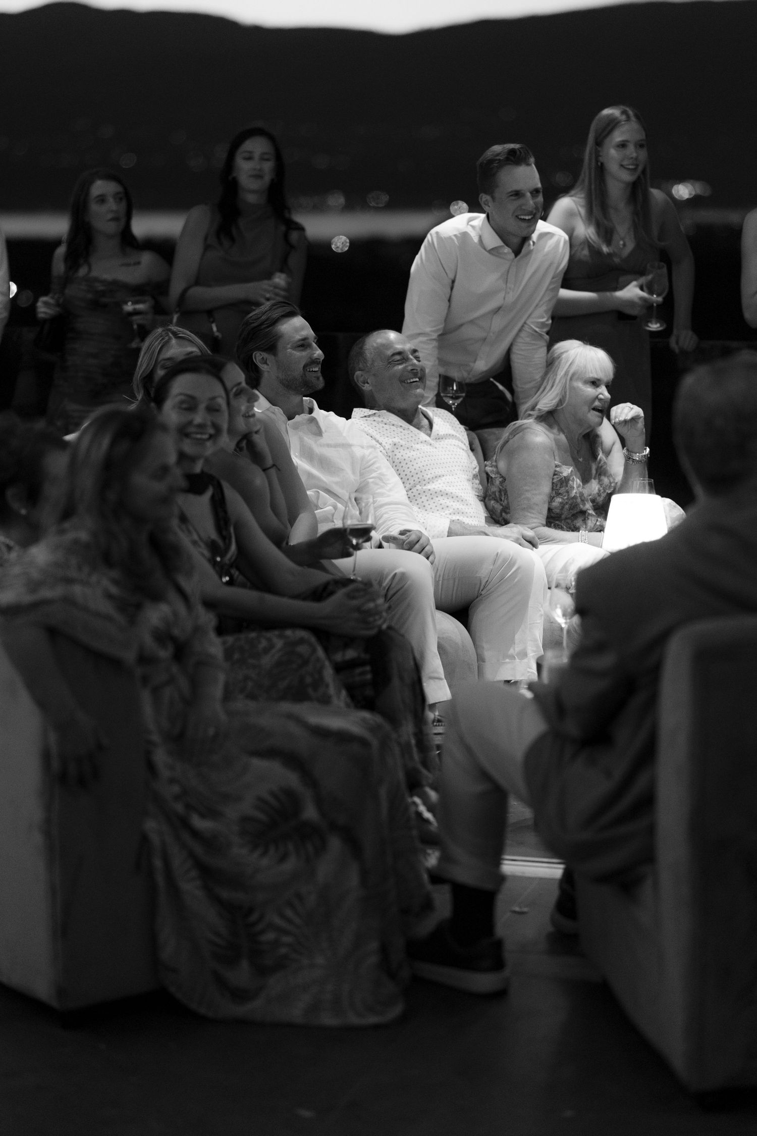 Black and white photo of wedding guests laughing and enjoying speeches at reception.