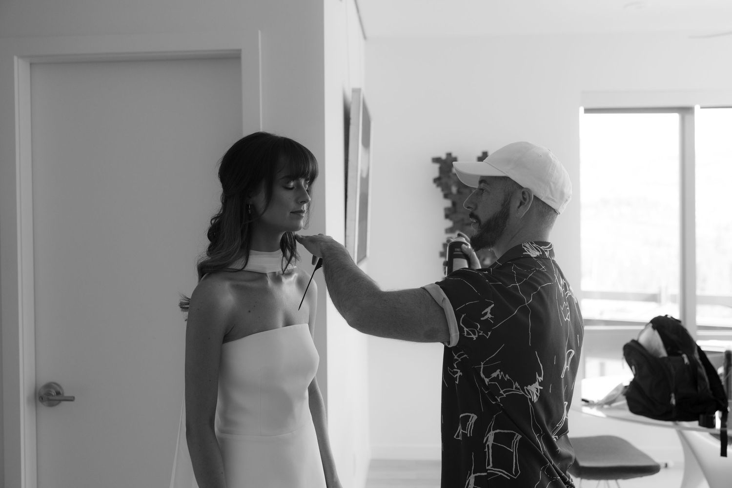 Black and white photo of stylist adjusting brides halter neckline dress before wedding ceremony.
