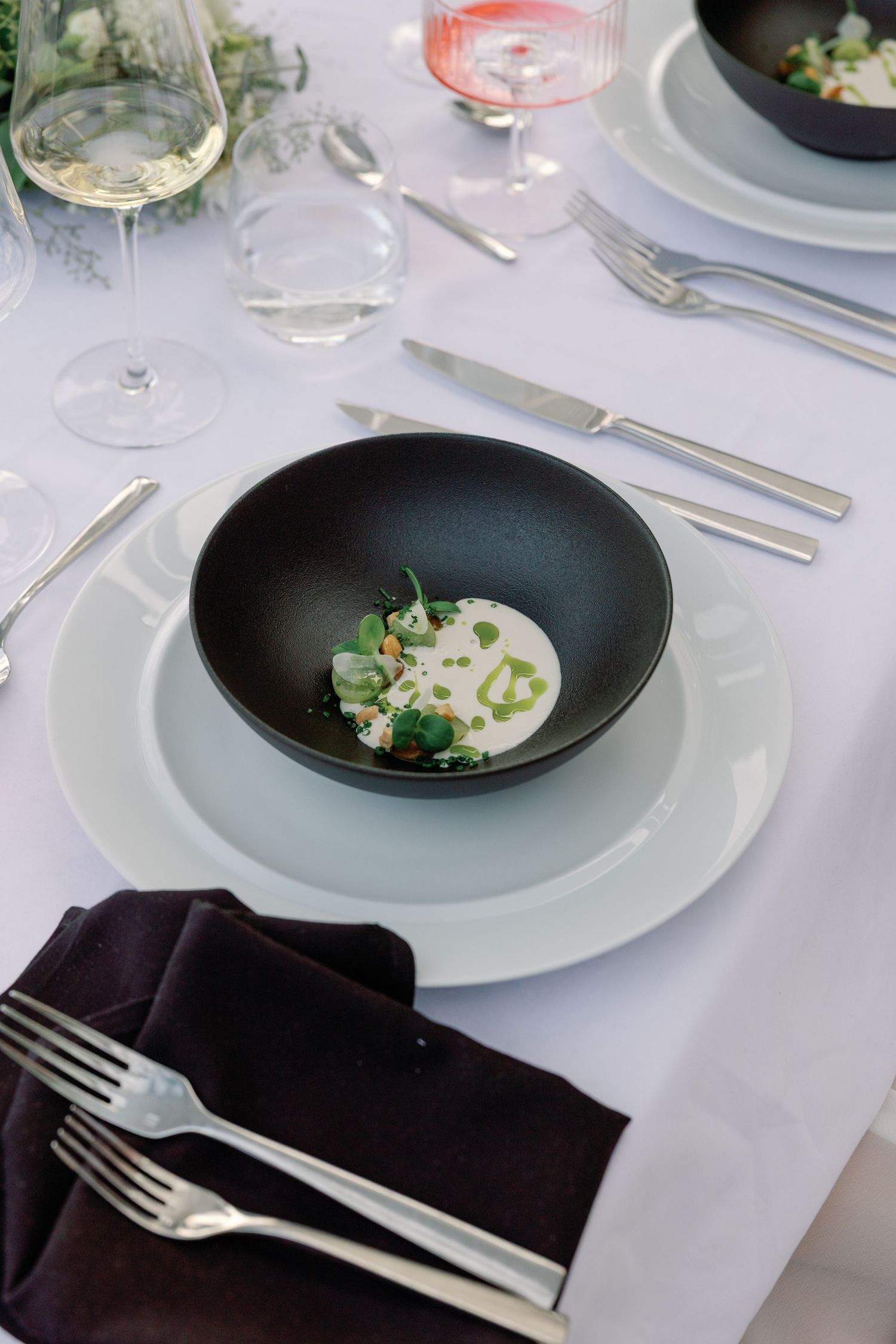 Artistic plated dish in black bowl with white sauce and microgreens on elegant wedding table.
