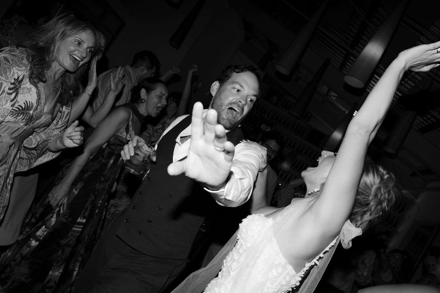 Black and white photo of bride and groom dancing energetically at wedding reception.