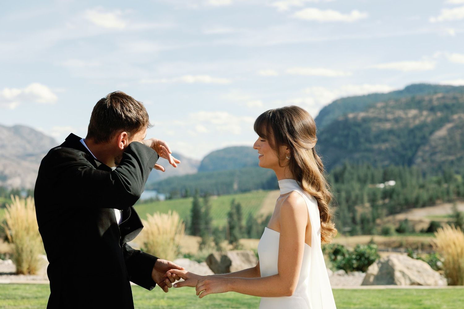 Groom emotionally reading vows while bride smiles during outdoor wedding ceremony with mountain backdrop.