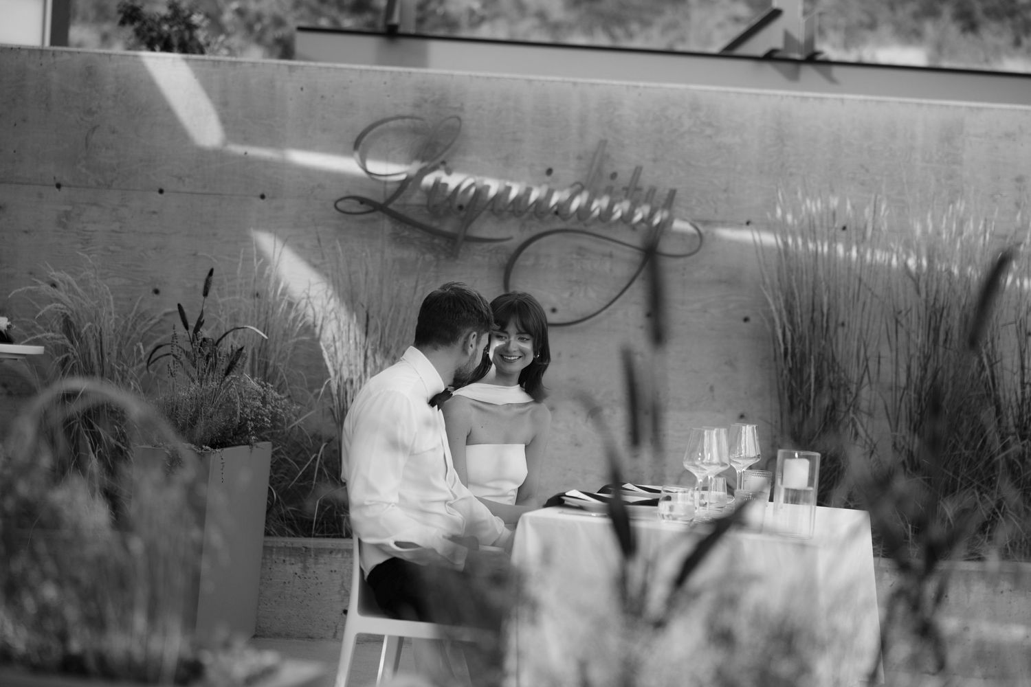 Bride and groom share intimate dinner moment at Liquidity Winery in black and white photo.