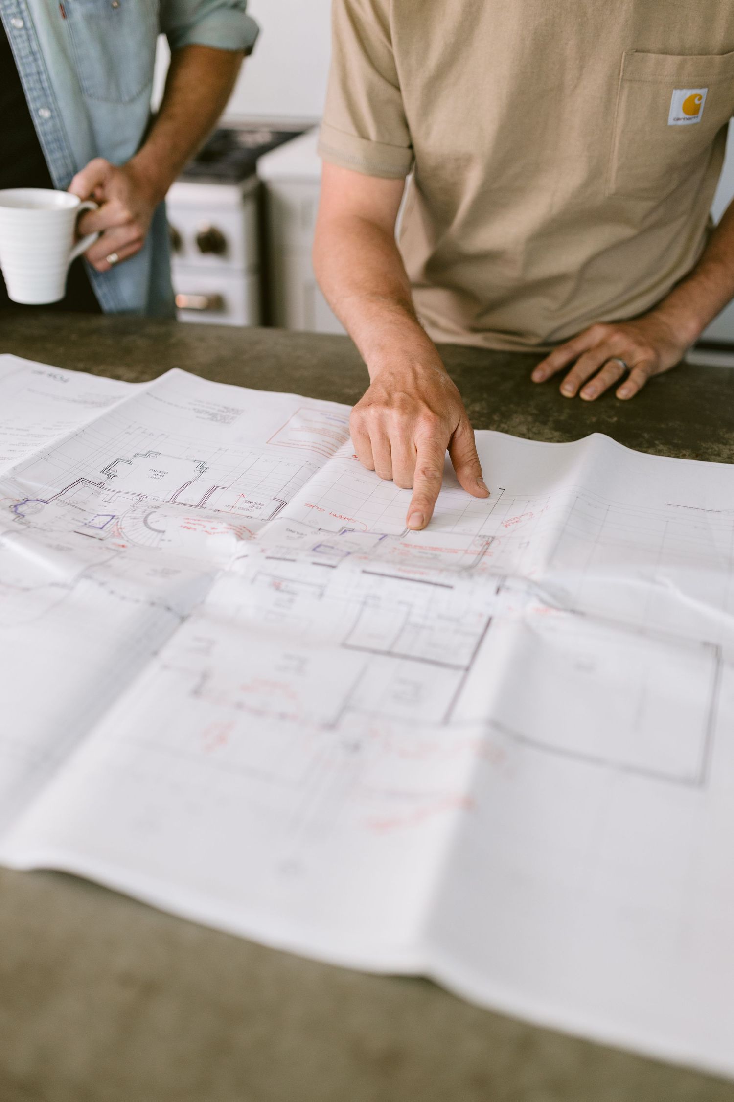 Two construction workers reviewing architectural blueprints spread on a table, one pointing at floor plans.