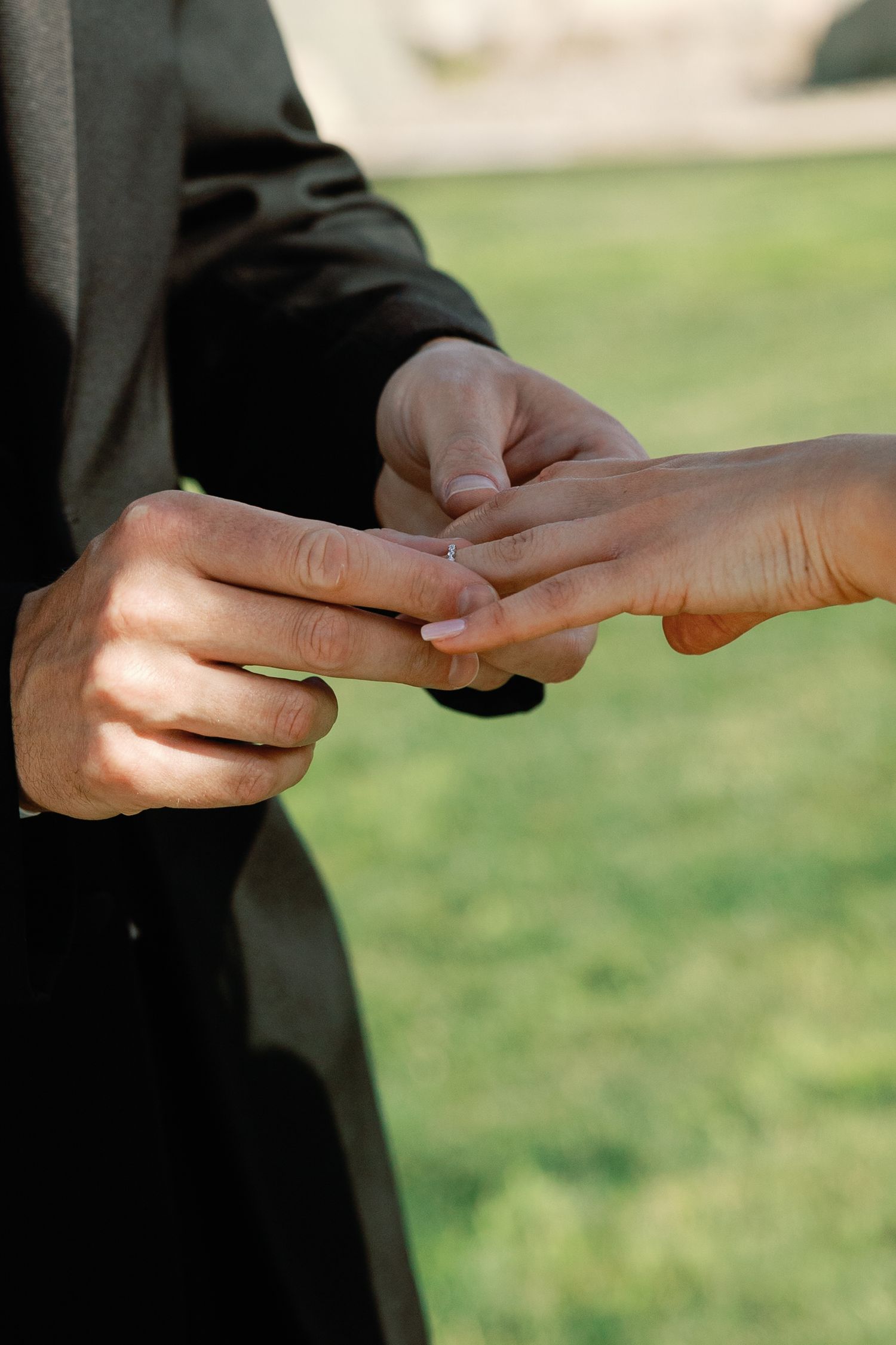 Groom places wedding ring on brides finger during outdoor ring exchange ceremony.