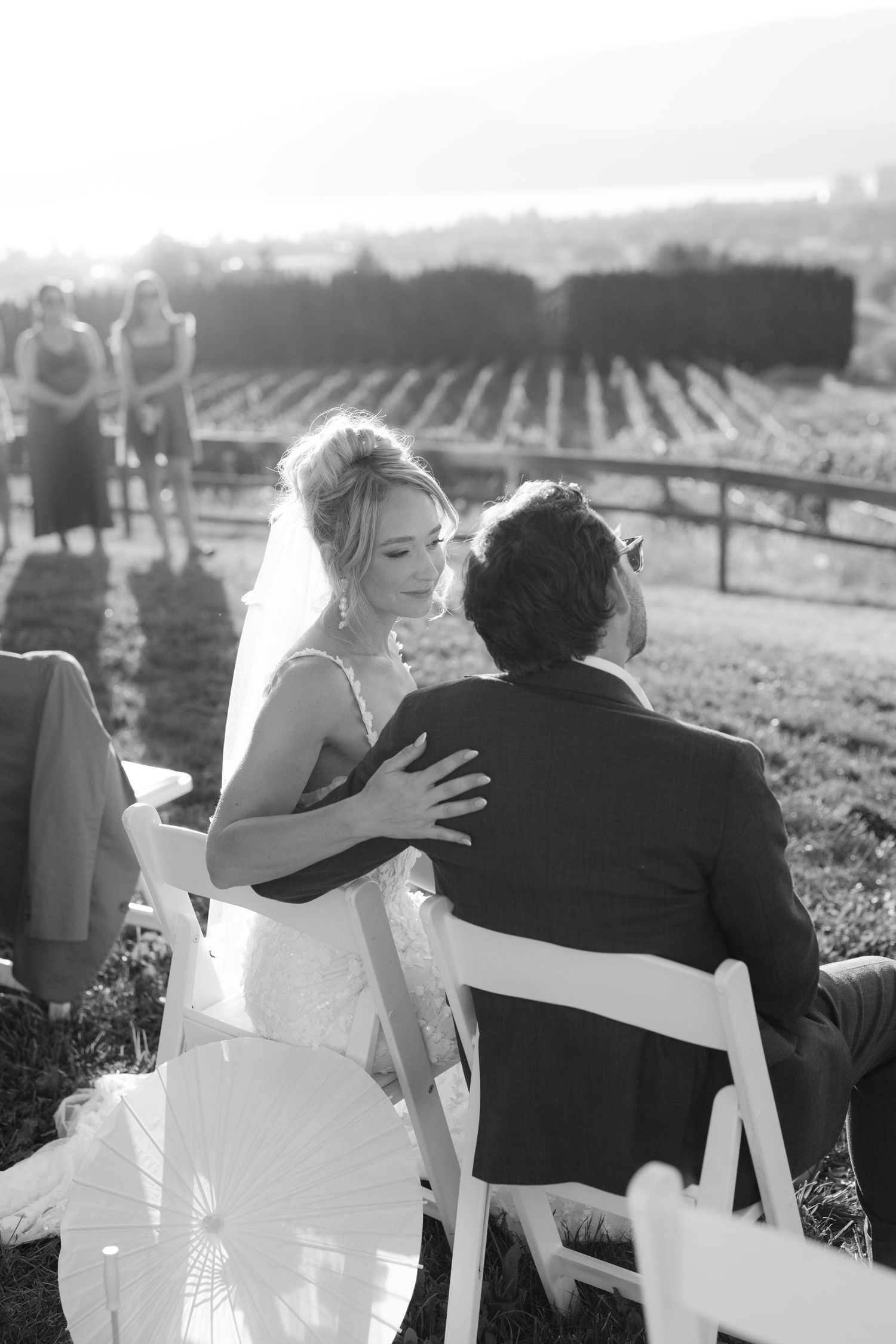 Black and white photo of bride in veil touching grooms shoulder at vineyard wedding ceremony.