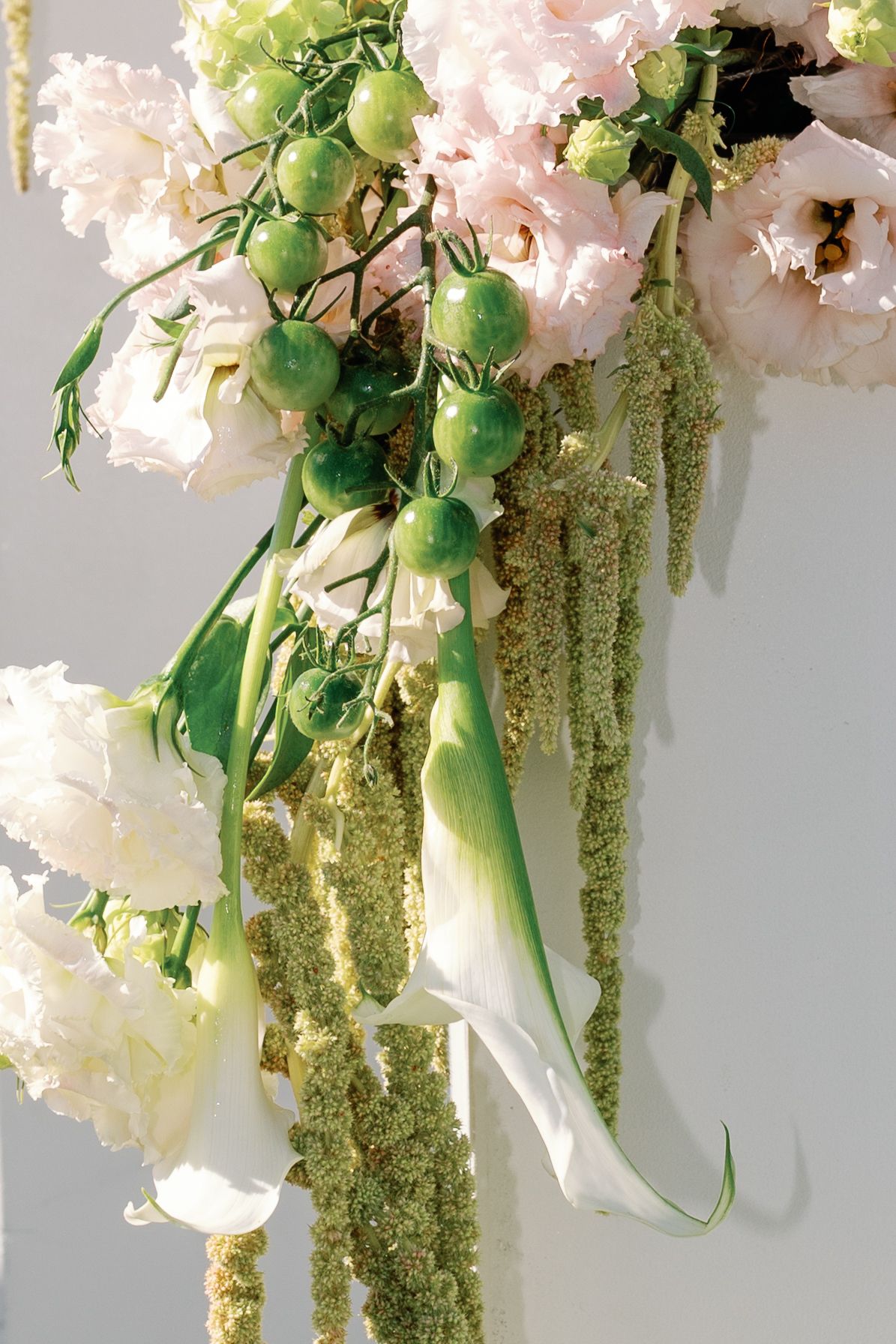 Close-up of cascading green amaranthus, cherry tomatoes, and blush flowers in wedding arrangement.