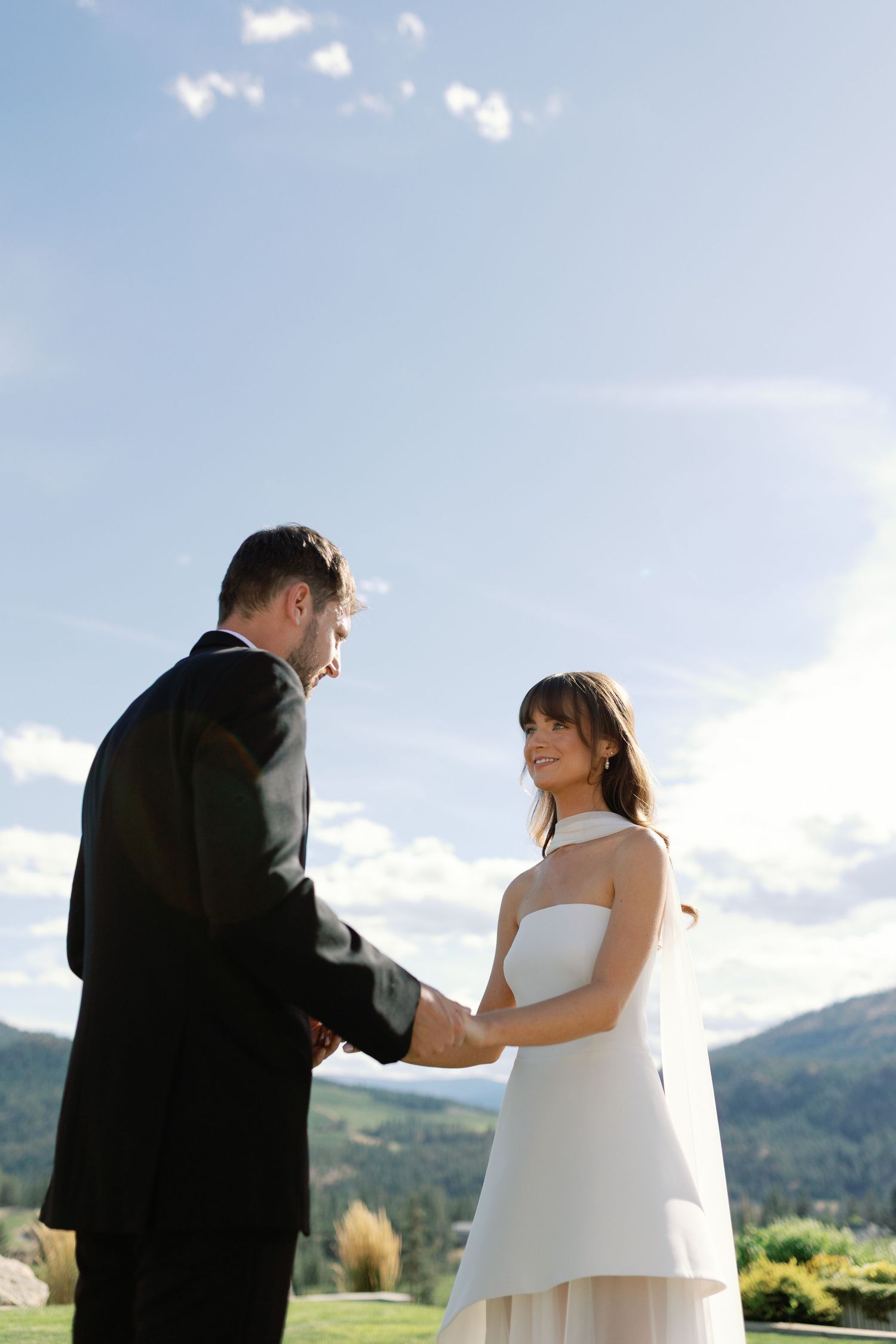 Bride and groom holding hands during outdoor wedding ceremony with mountain landscape behind.