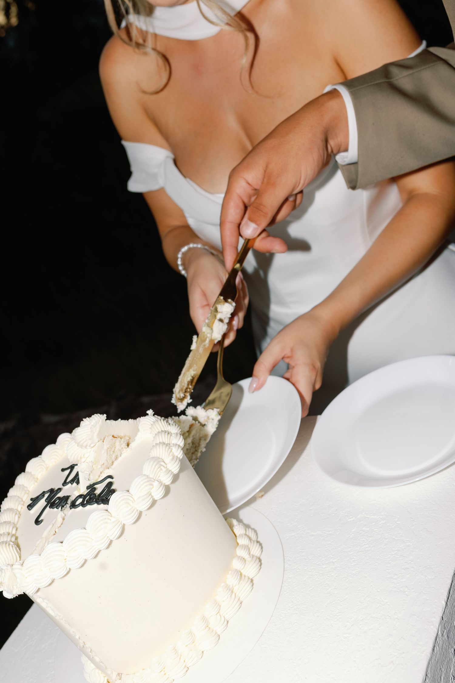 Bride and groom cutting a white wedding cake with pearl decorations and elegant script writing together.