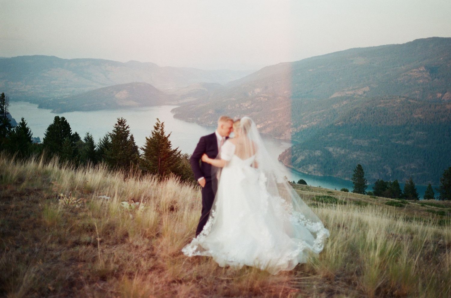 Bride and groom share a romantic dance on a hillside with a stunning lake and mountain backdrop.