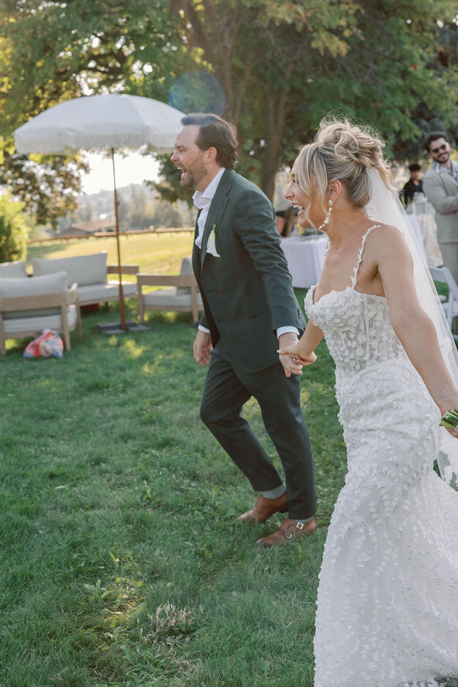 Happy bride and groom walk hand in hand laughing after outdoor wedding ceremony.