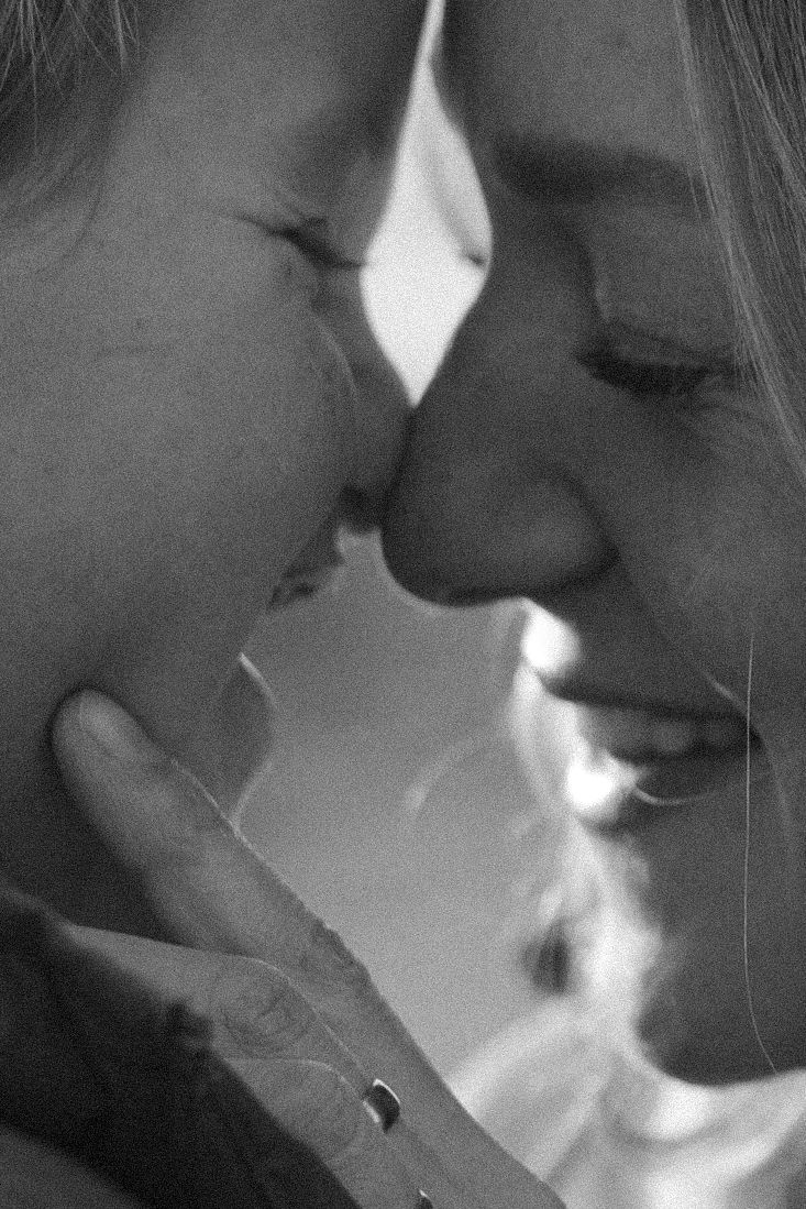 Black and white photo of two people smiling and touching foreheads in an intimate, tender moment.