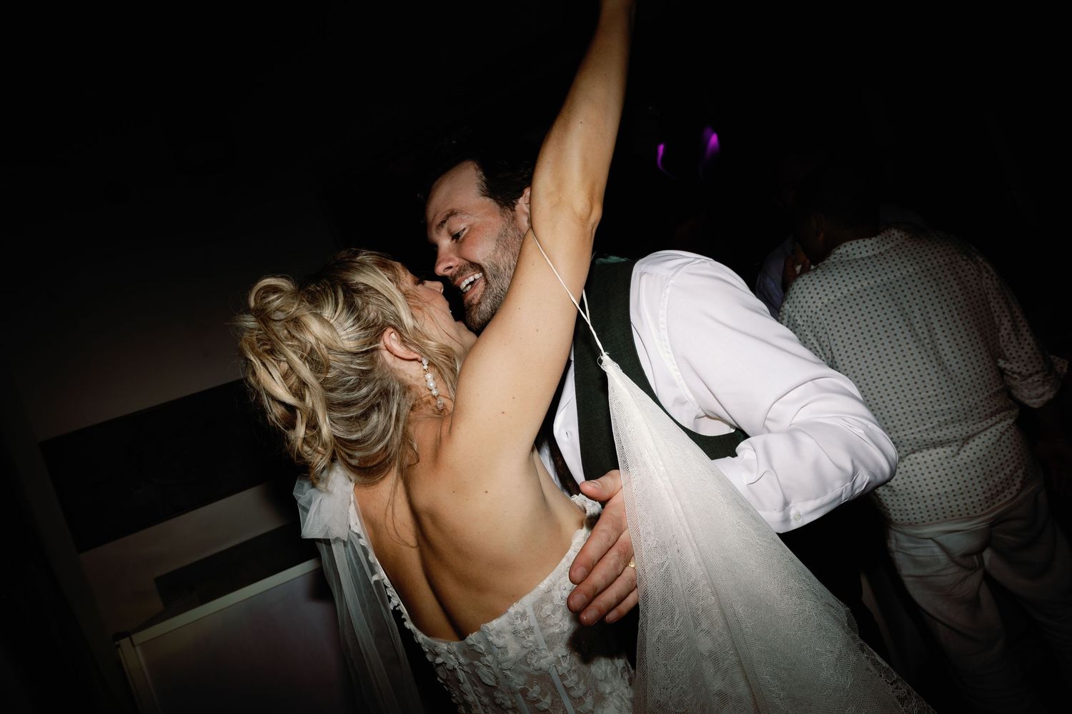 Bride and groom dance closely together in dramatic lighting at wedding reception.