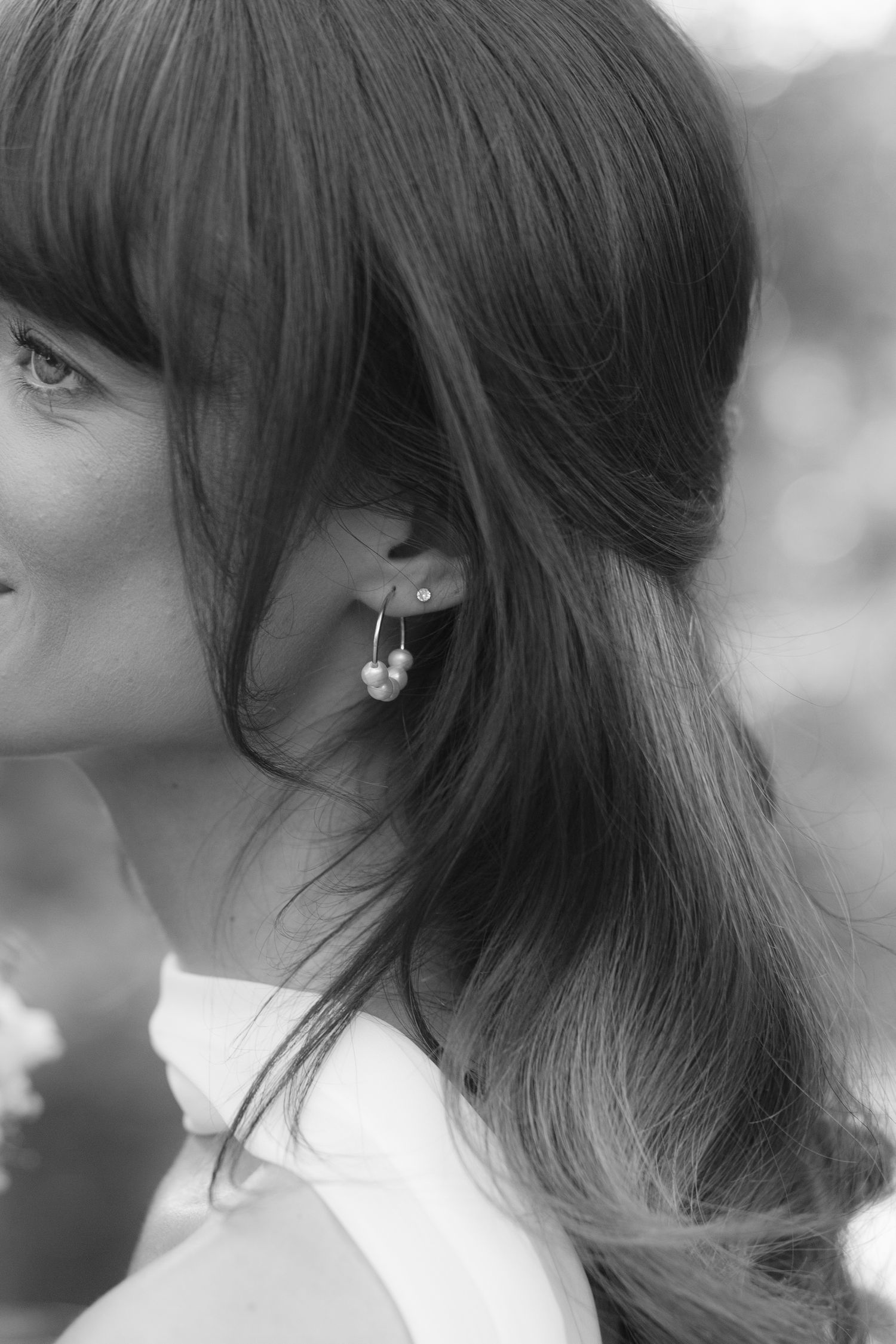 Black and white close-up portrait of bride with elegant pearl drop earrings and flowing dark hair at wedding.
