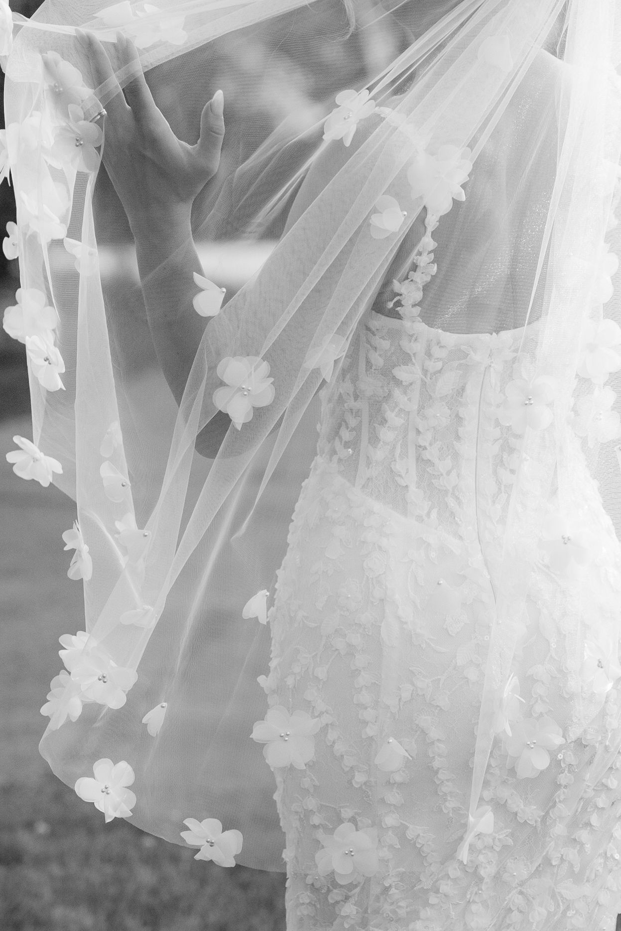 Black and white close-up of bride in floral applique gown and delicate veil.